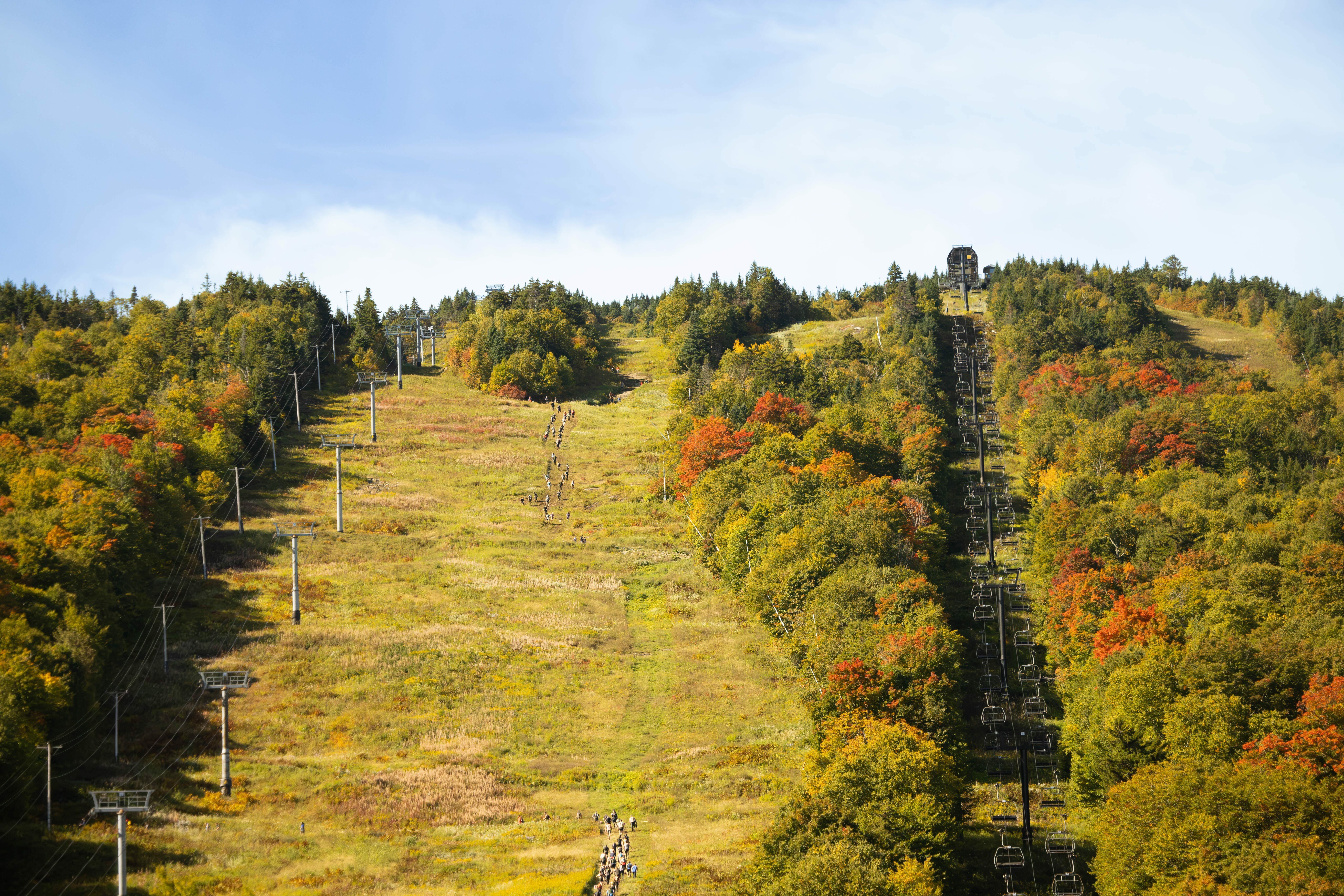 A hillside with ski lift, colorful trees, and people hiking in autumn scenery.