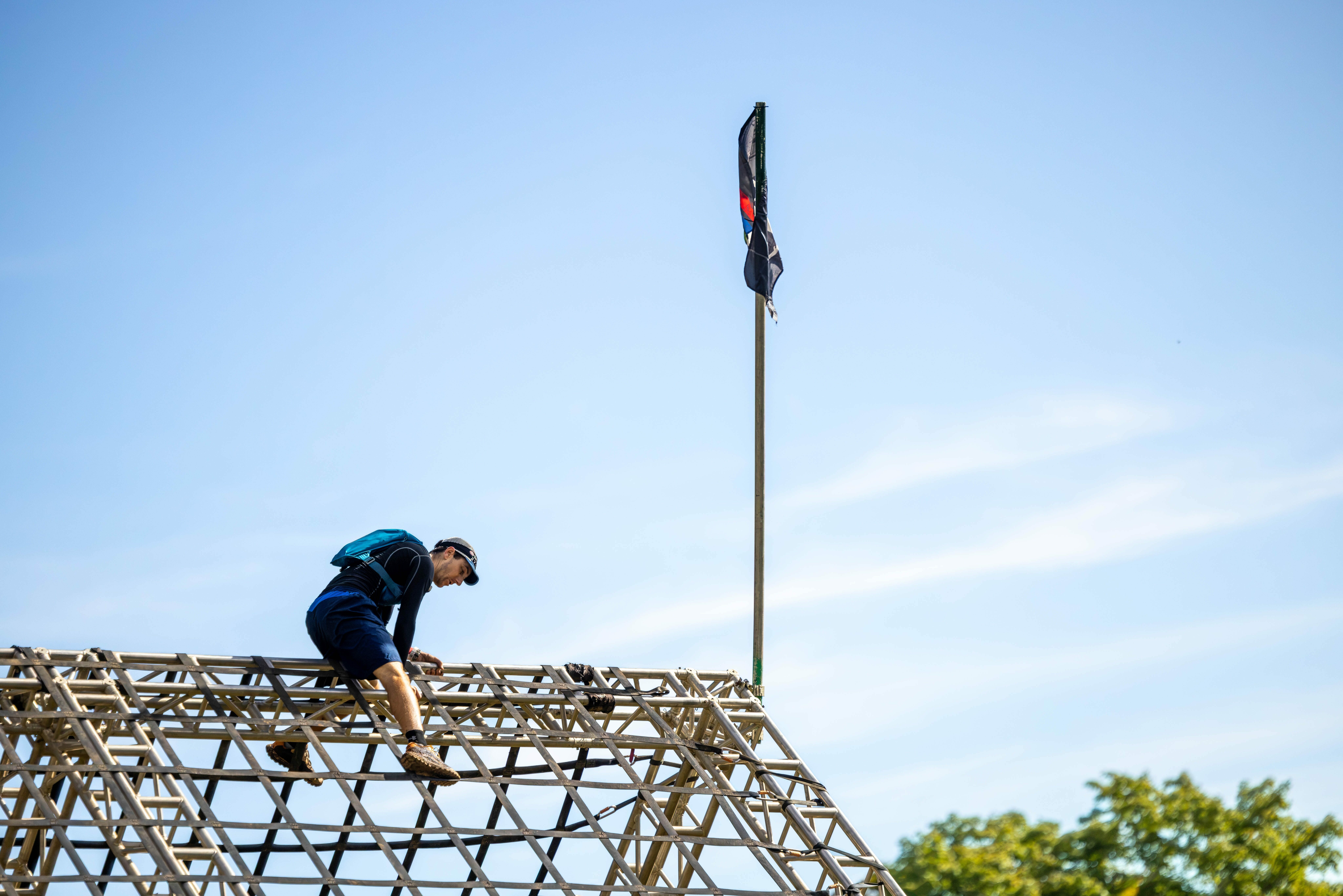 A person climbs a structure under a clear blue sky, with a flag visible above.