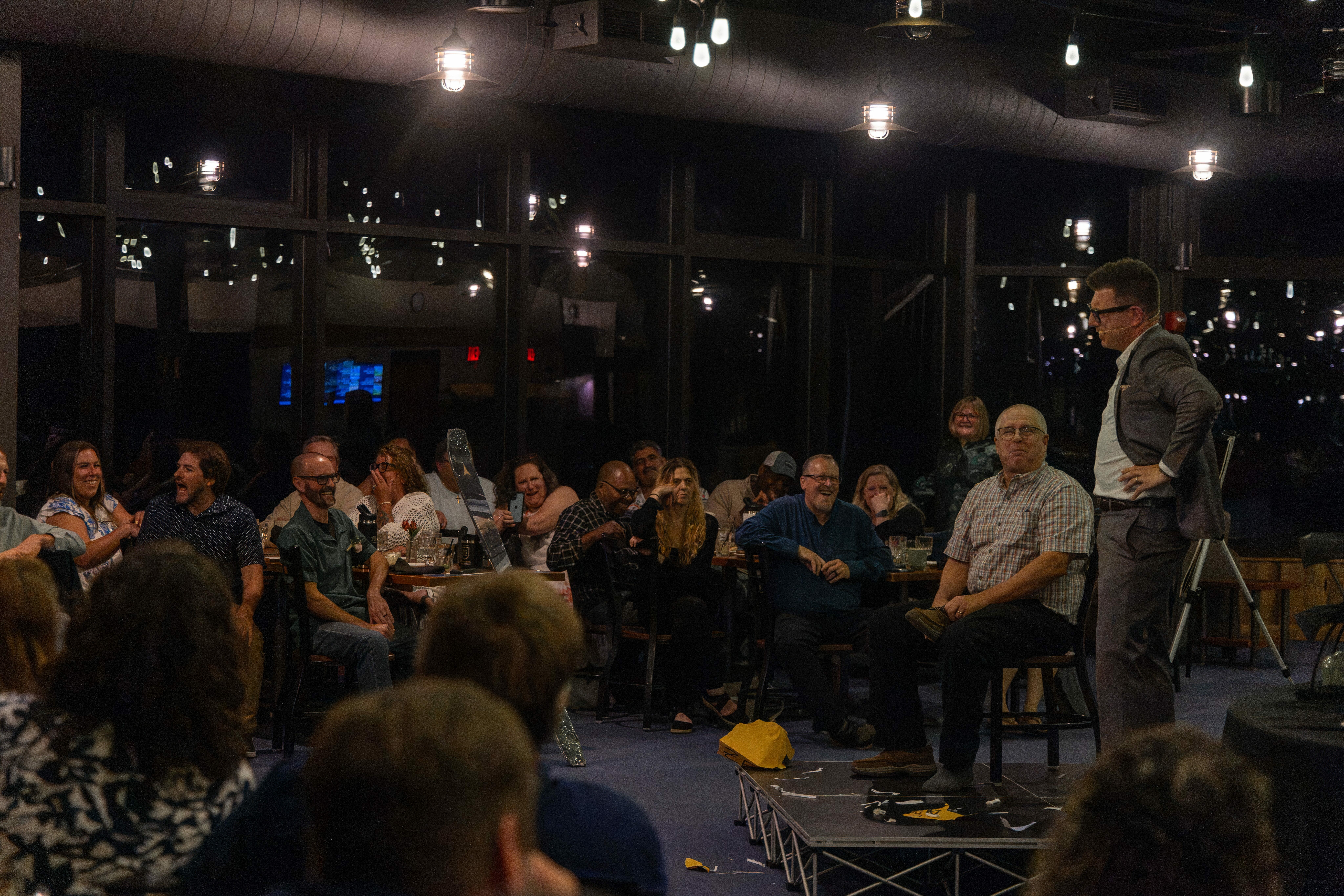 A magician performs in a lively venue, engaging an amused audience.