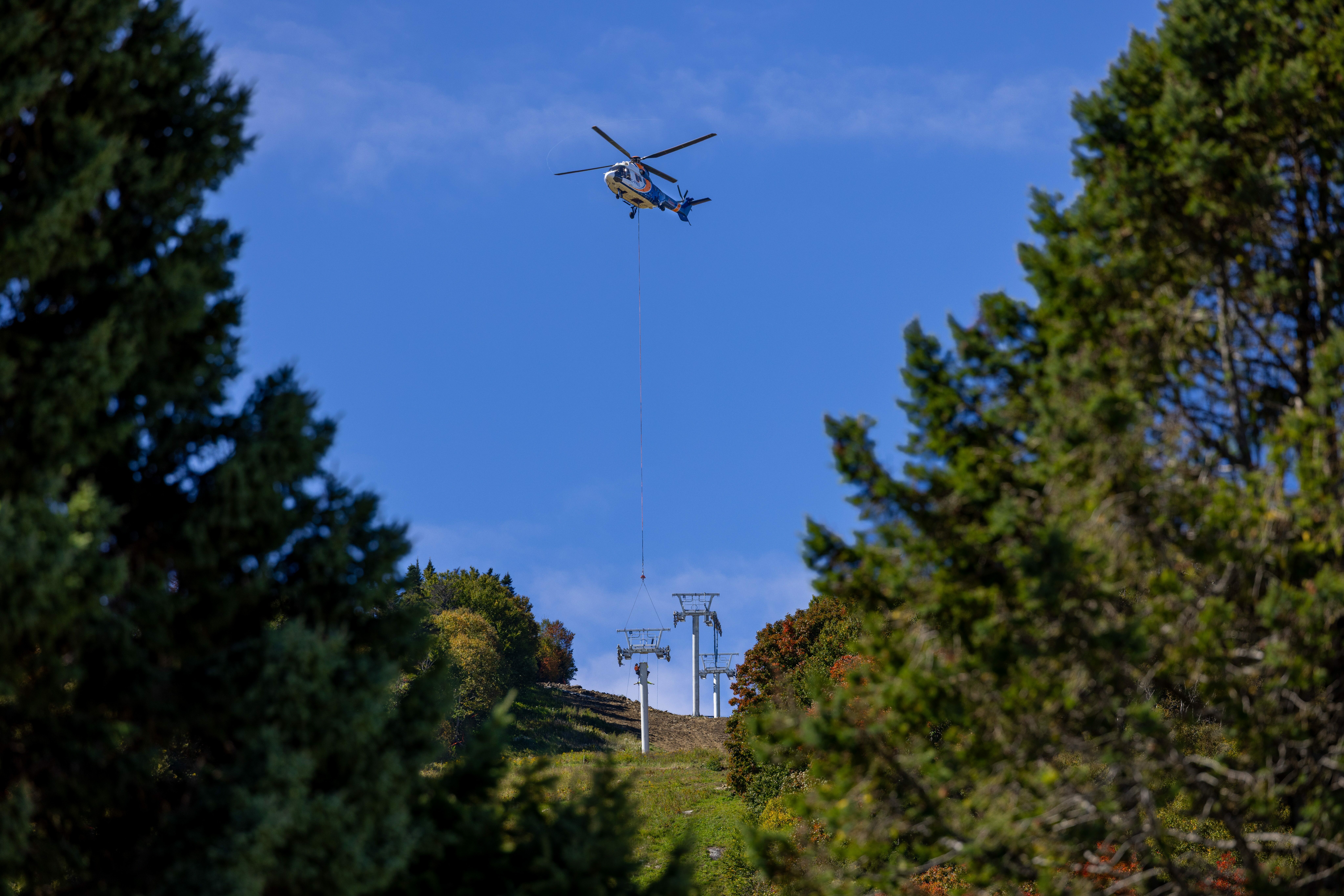 Helicopter lifting objects near ski lift towers against a clear blue sky.