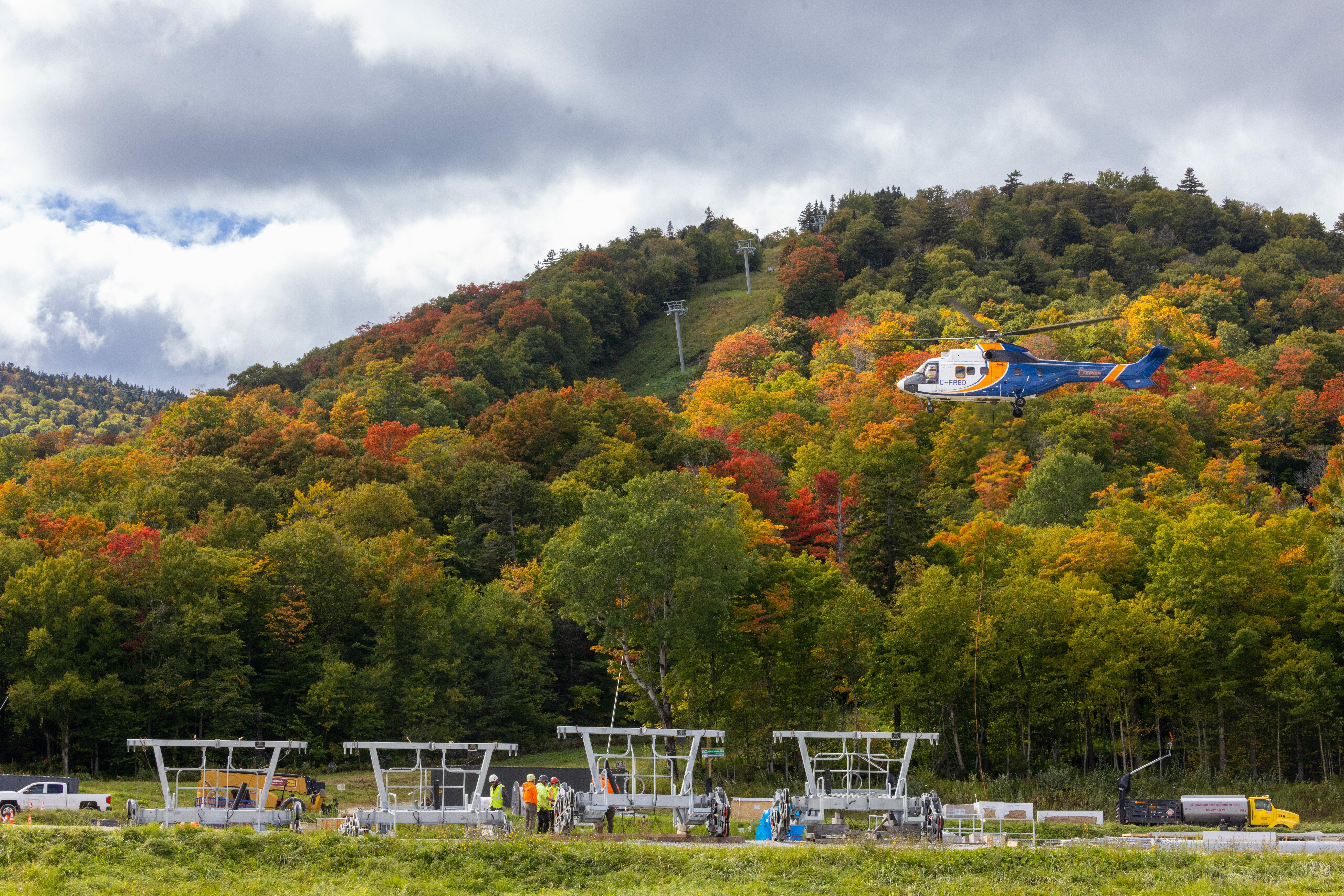 Helicopter flying over colorful autumn foliage and construction equipment below.