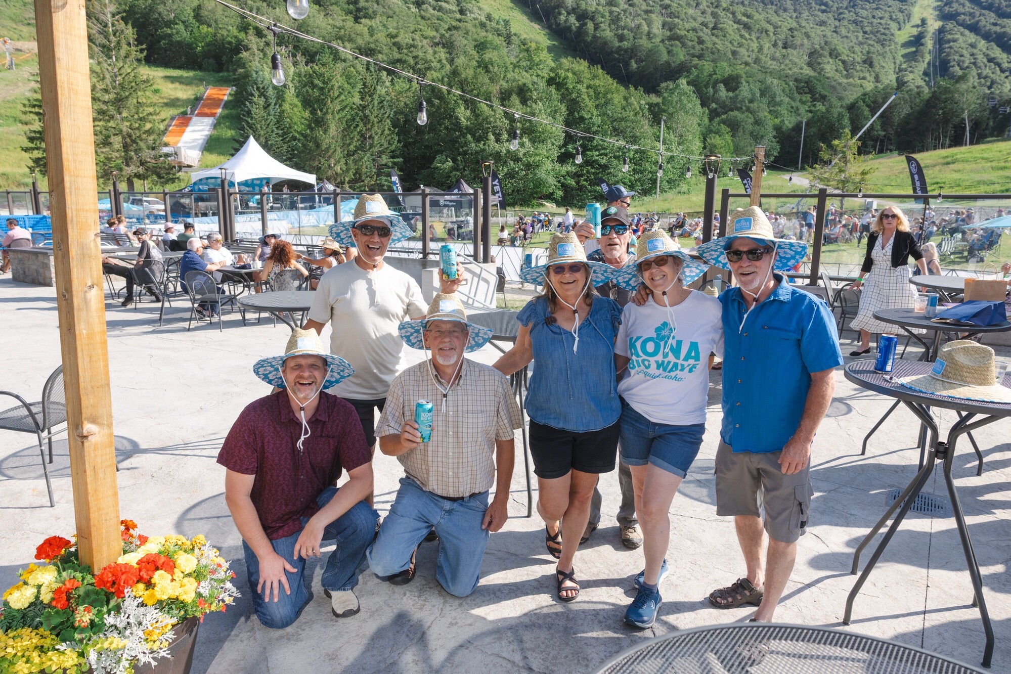 A group of six people in hats posing together outdoors at a sunny event.