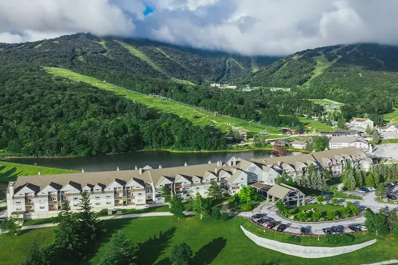 Aerial view of a resort by a lake, surrounded by mountains and greenery.