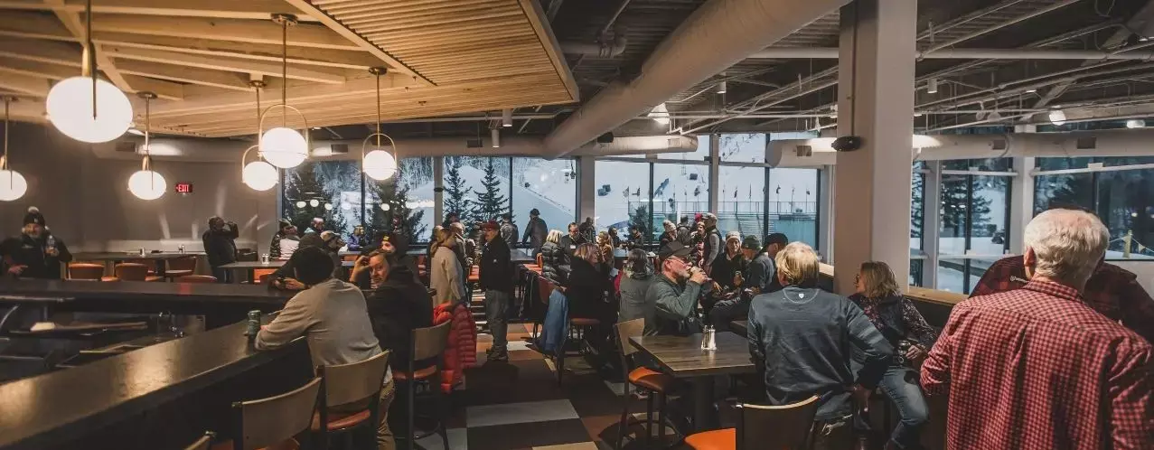 Crowded caf&eacute; with patrons socializing, large windows showing a snowy outdoor scene.
