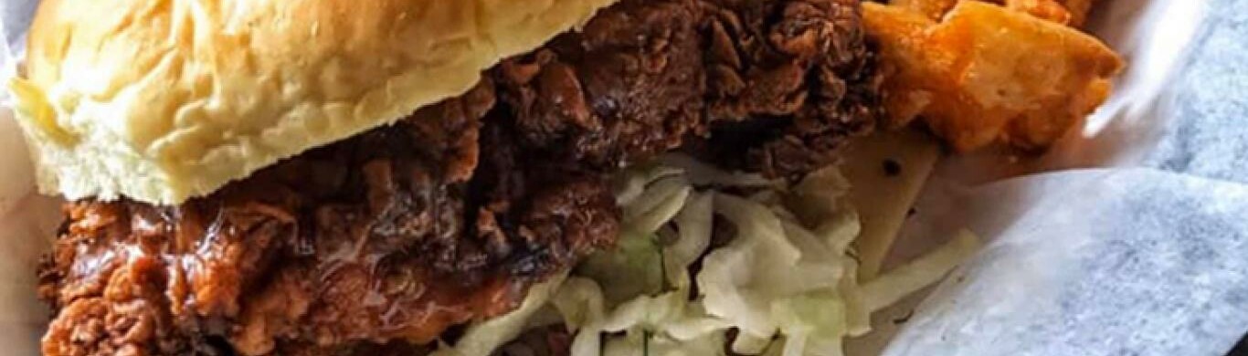 Close-up of a fried chicken sandwich with lettuce and fried sides.