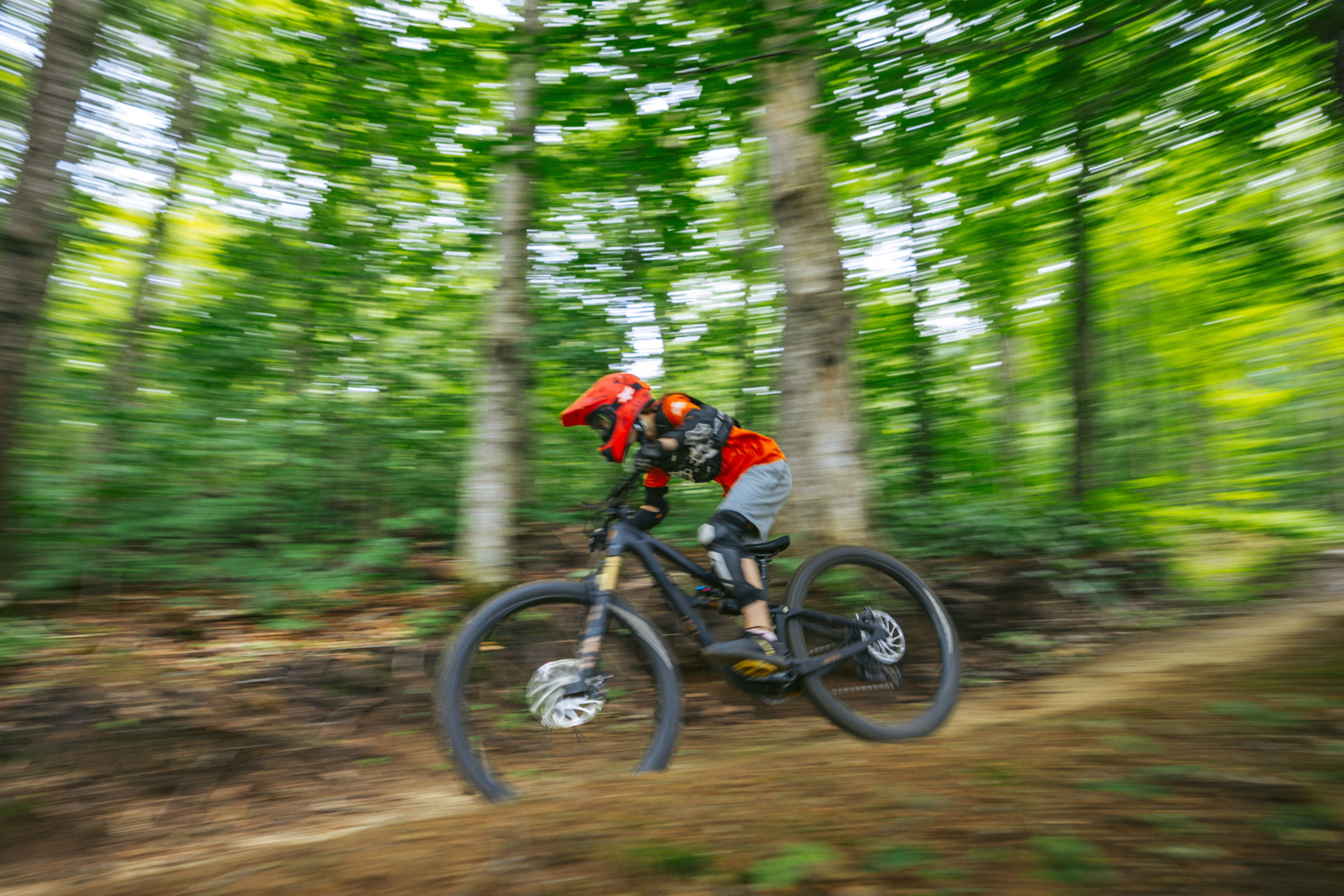 A biker in a red helmet speeds down a forest dirt trail.