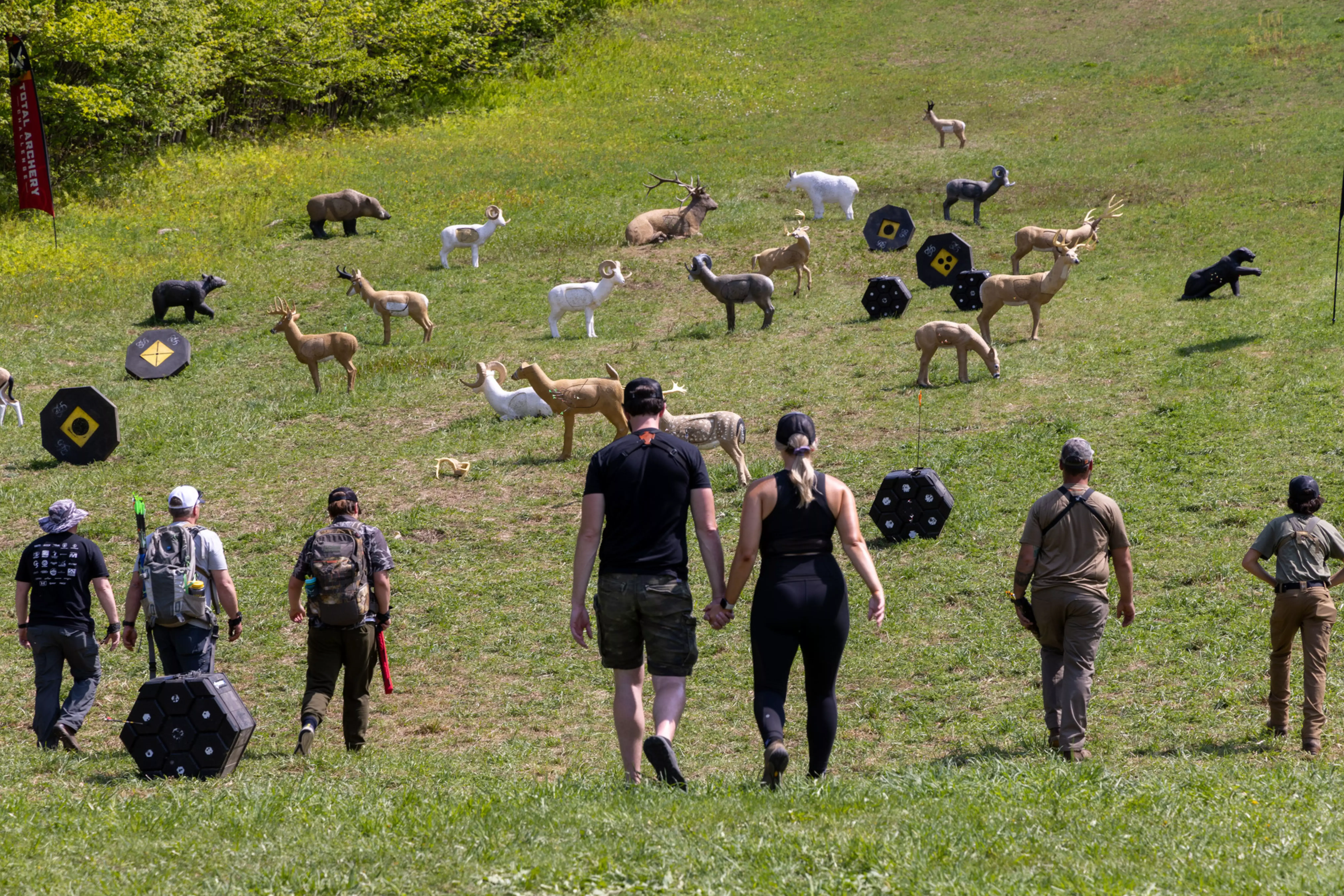 A couple walks hand in hand towards archery targets on a grassy field.