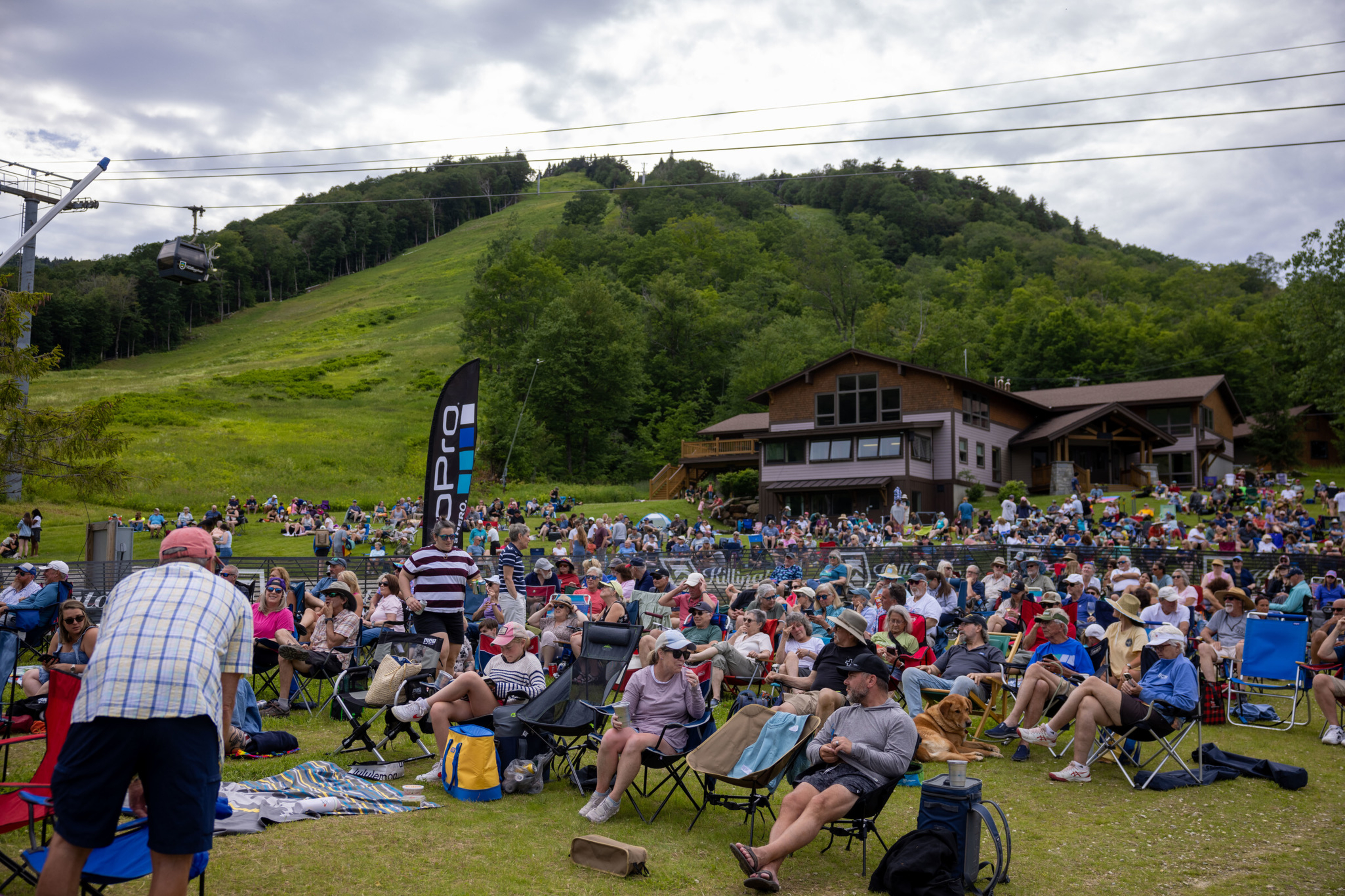 Crowd seated on lawn chairs at an outdoor event with a mountain backdrop.