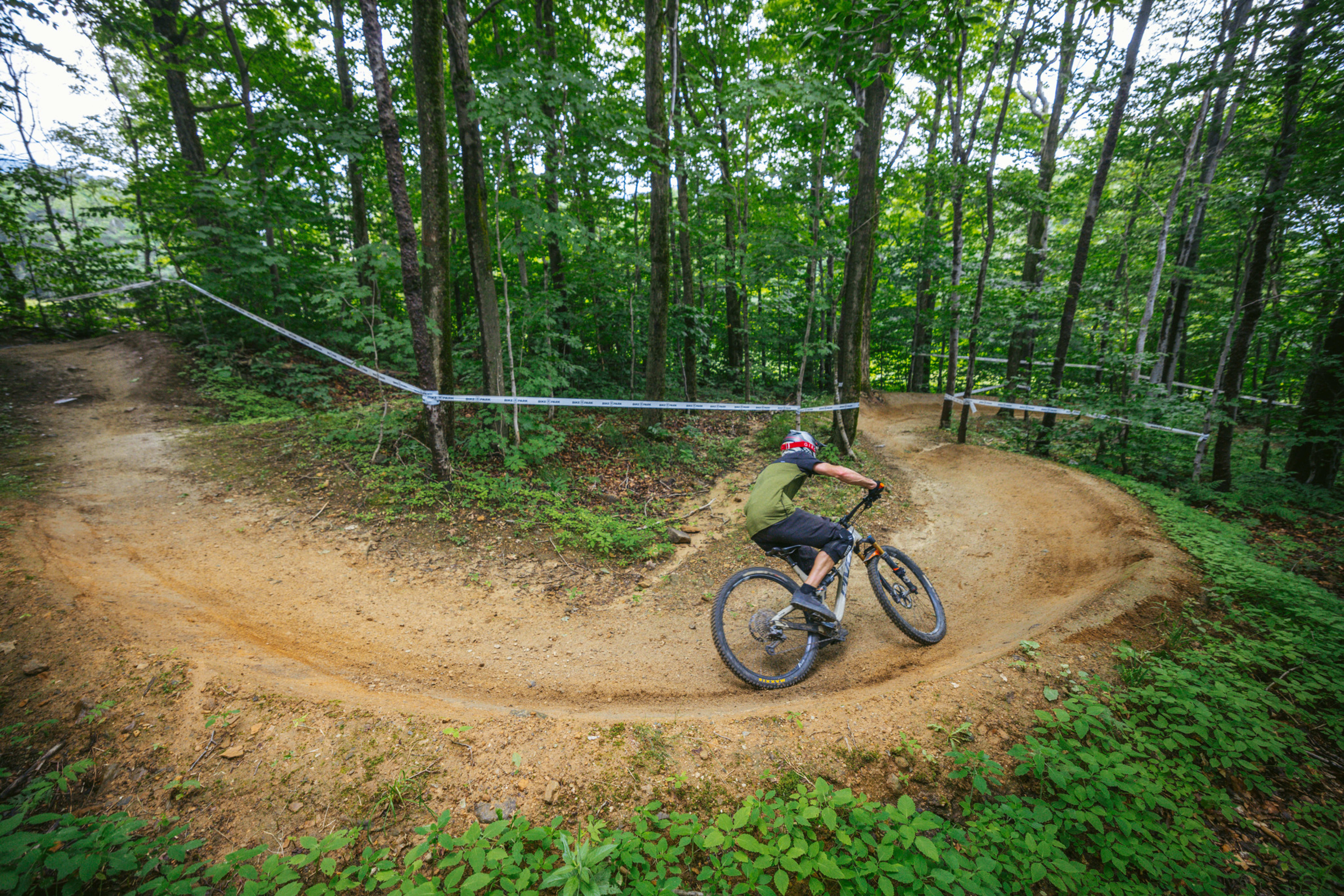 A mountain biker navigates a curved dirt trail in a lush forest.