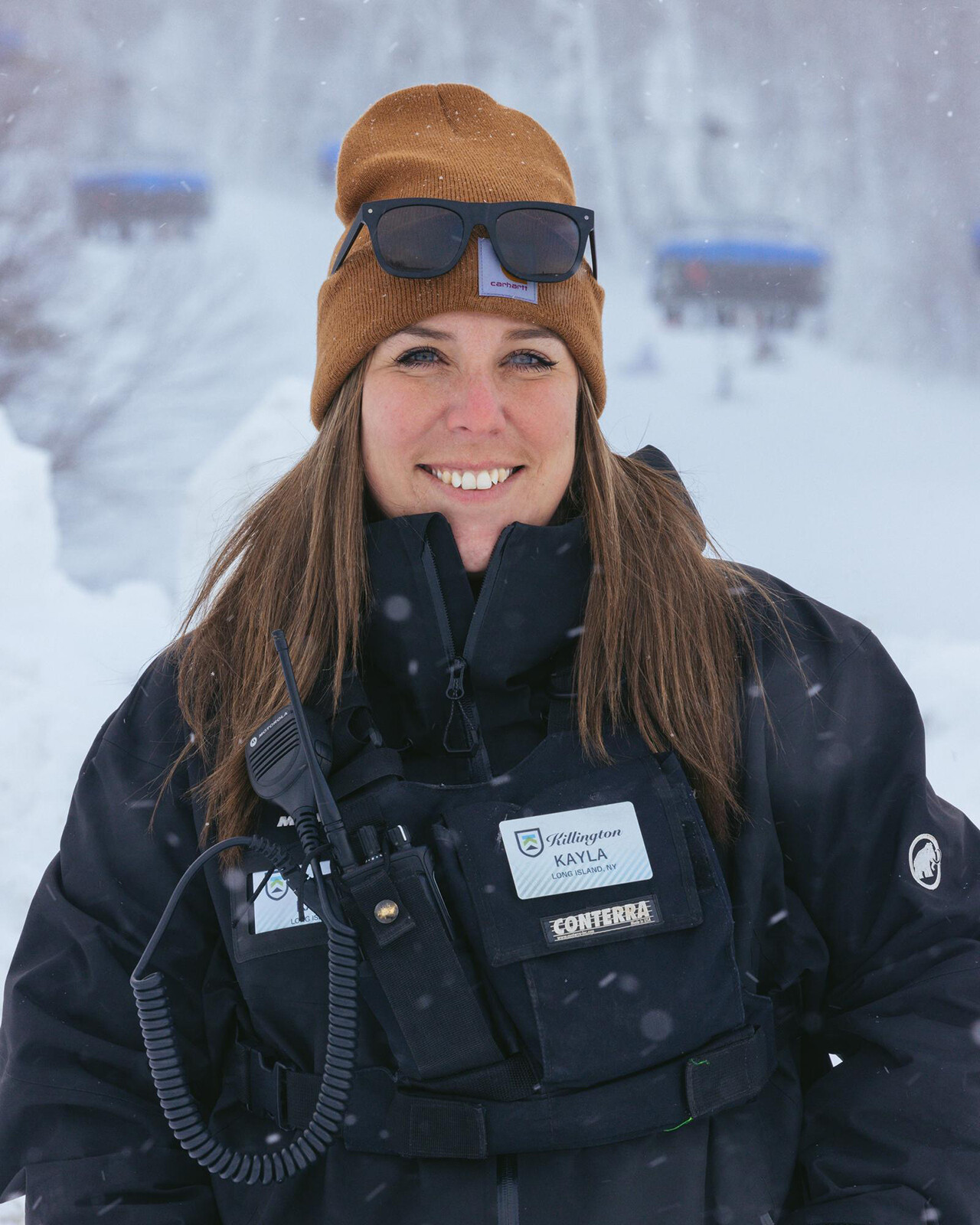 A woman in a winter jacket and beanie smiles, snowflakes falling around her.