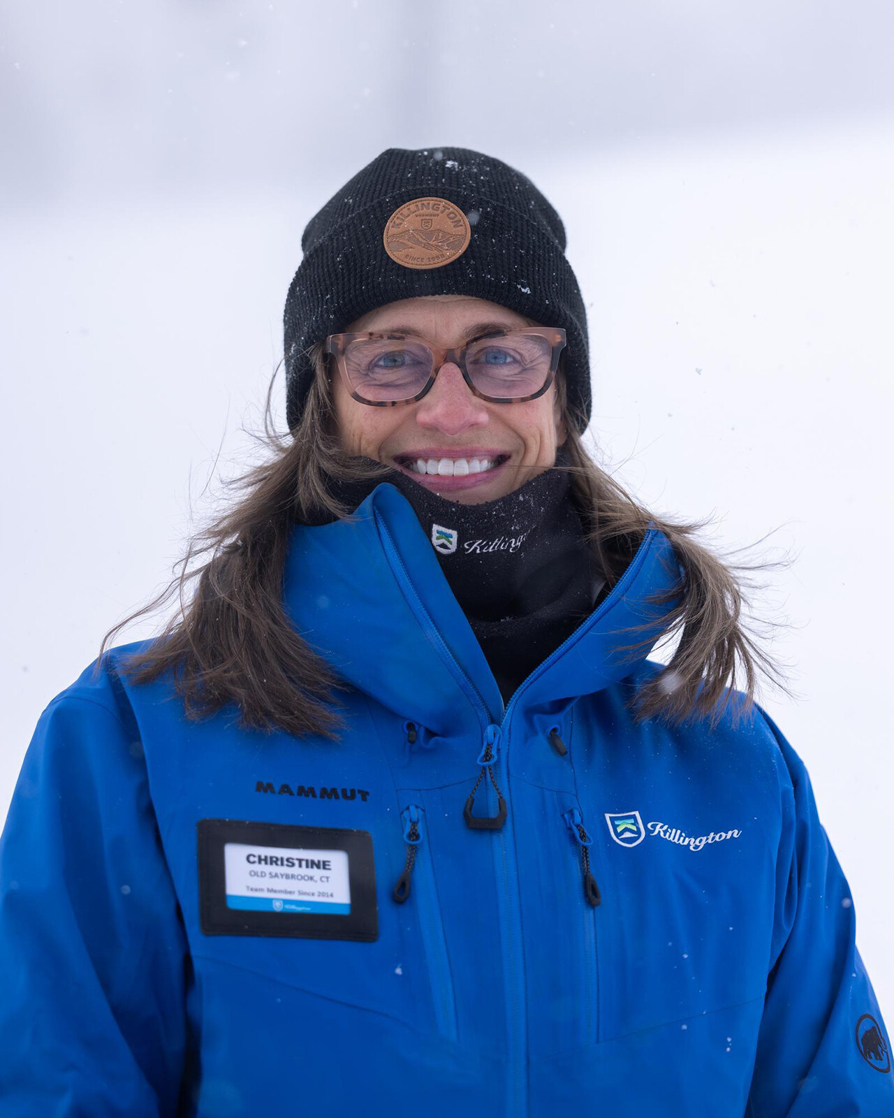 Smiling woman in a blue jacket and hat, outdoors in snowy weather.