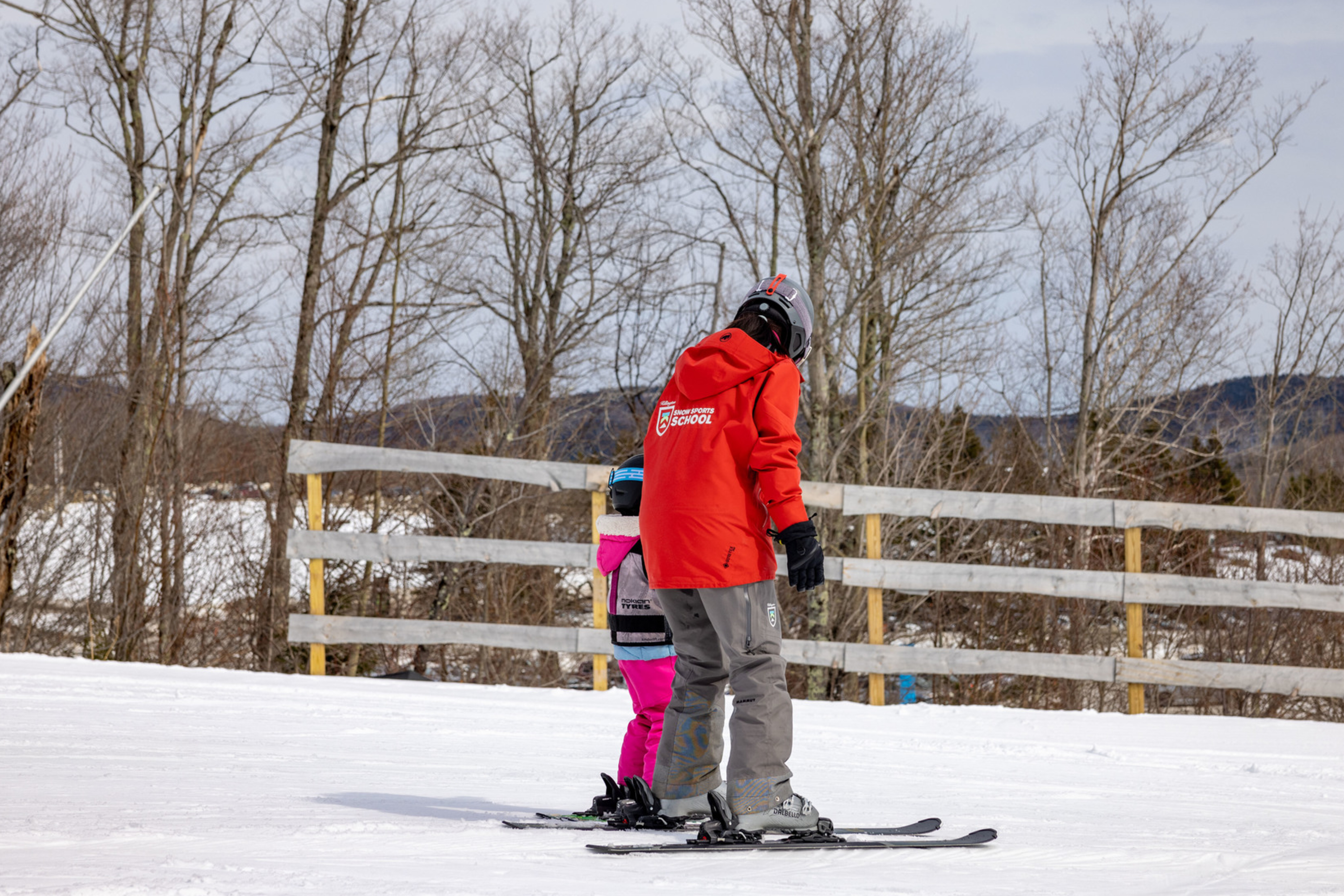 A ski instructor guides a child on skis in a snowy landscape.