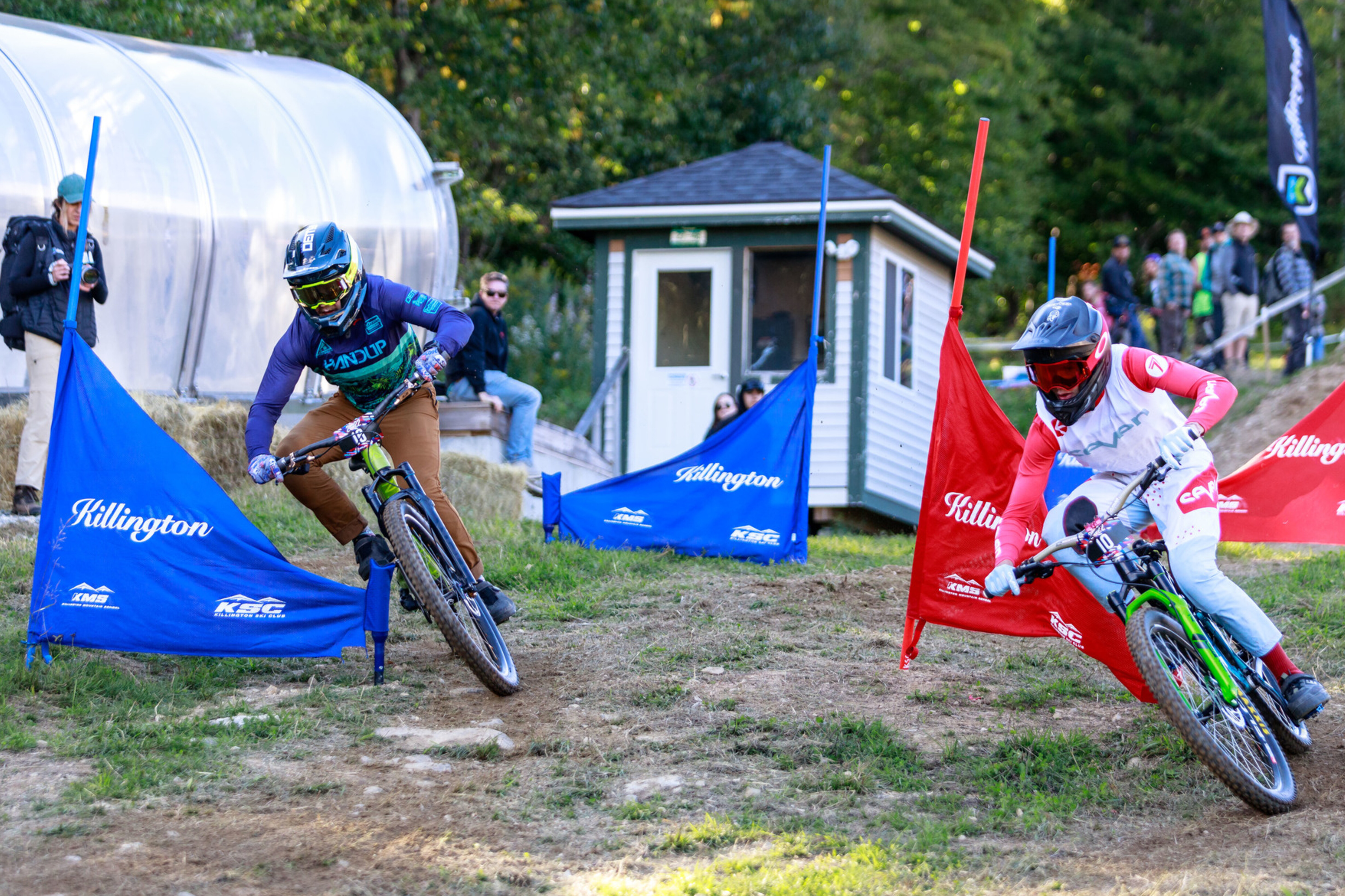 Two mountain bikers racing around colorful flags at a downhill event in Killington.