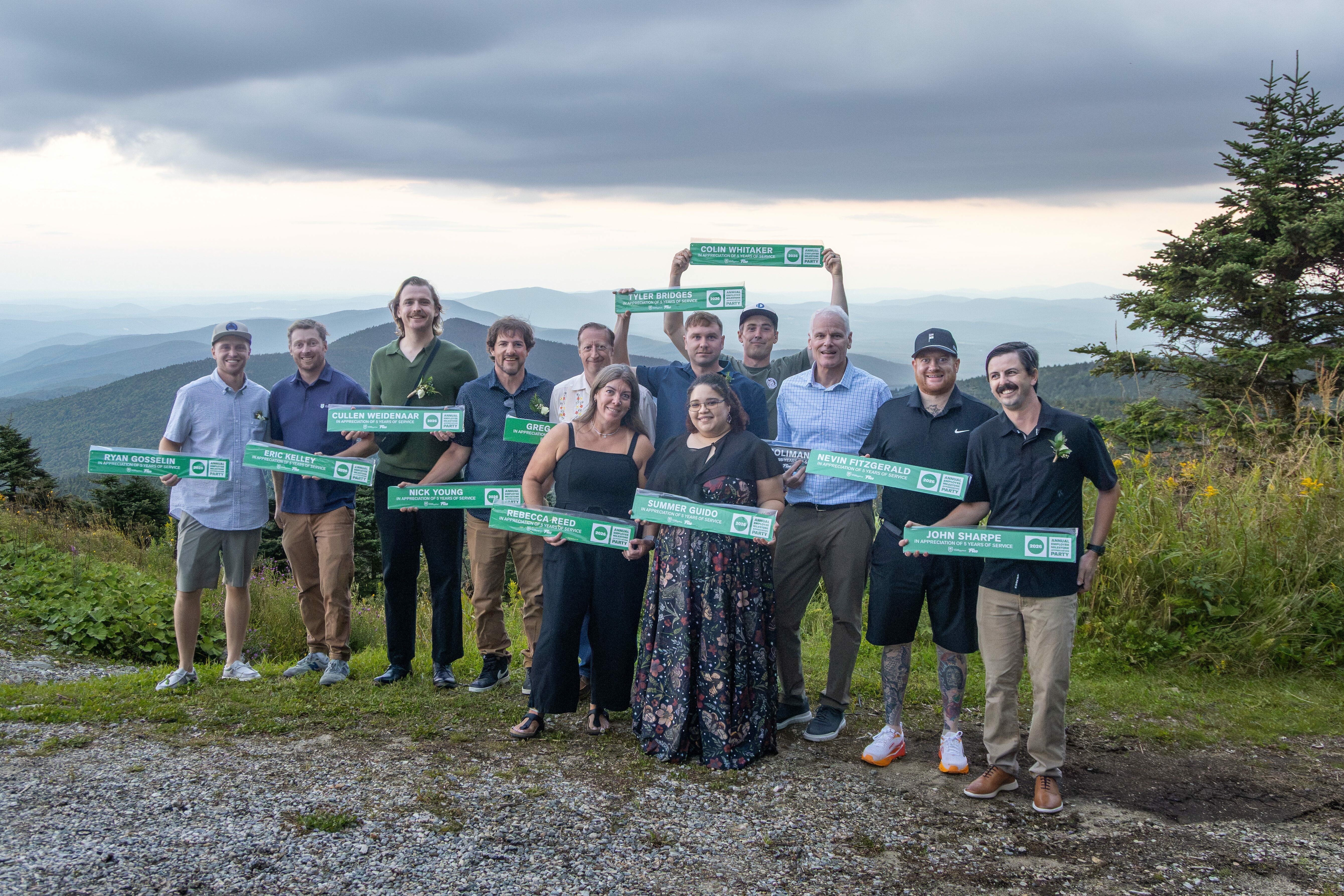 Group photo of 12 people holding signs in front of a mountain landscape.