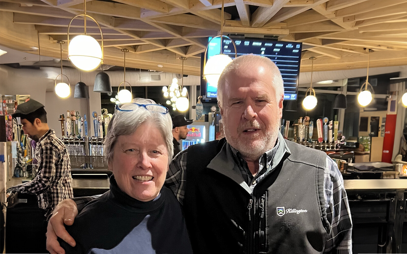 Two people smile for a photo in a bar with beer taps in the background.