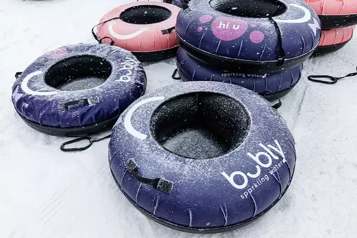Colorful snow tubes with branding, dusted with snow, stacked on a snowy surface.