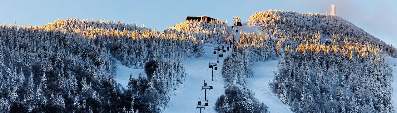 Snow-covered mountains with a ski lift and frosted trees basking in golden sunlight.