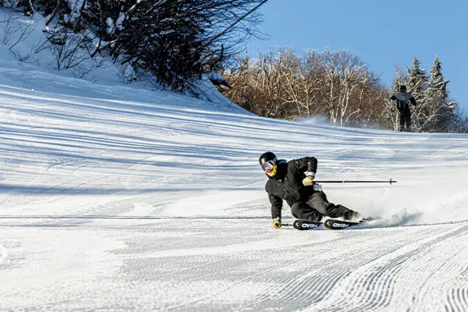 A skier carves down a snowy slope under a clear blue sky.