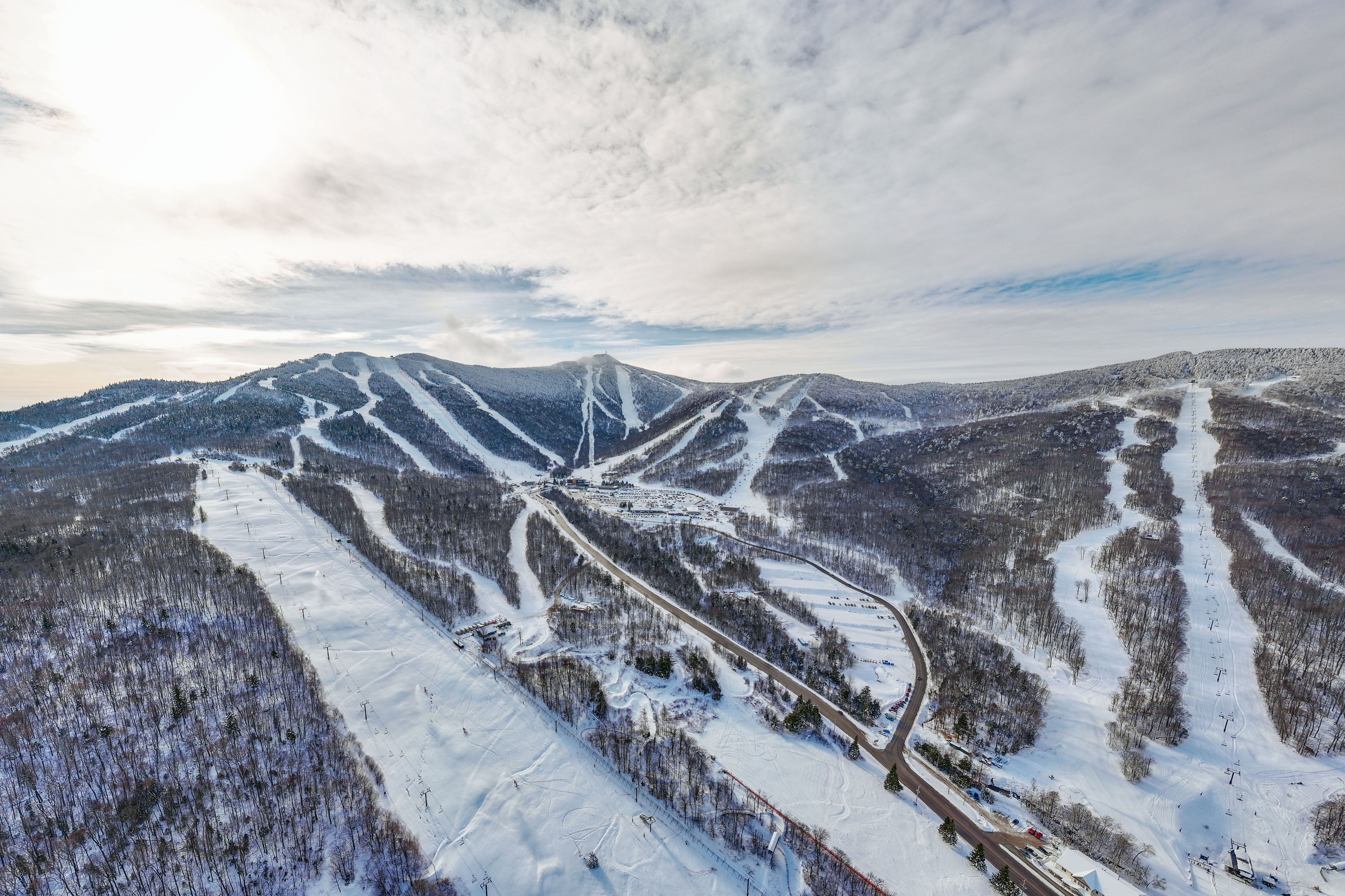 Aerial view of snow-covered mountains and ski slopes under a cloudy sky.