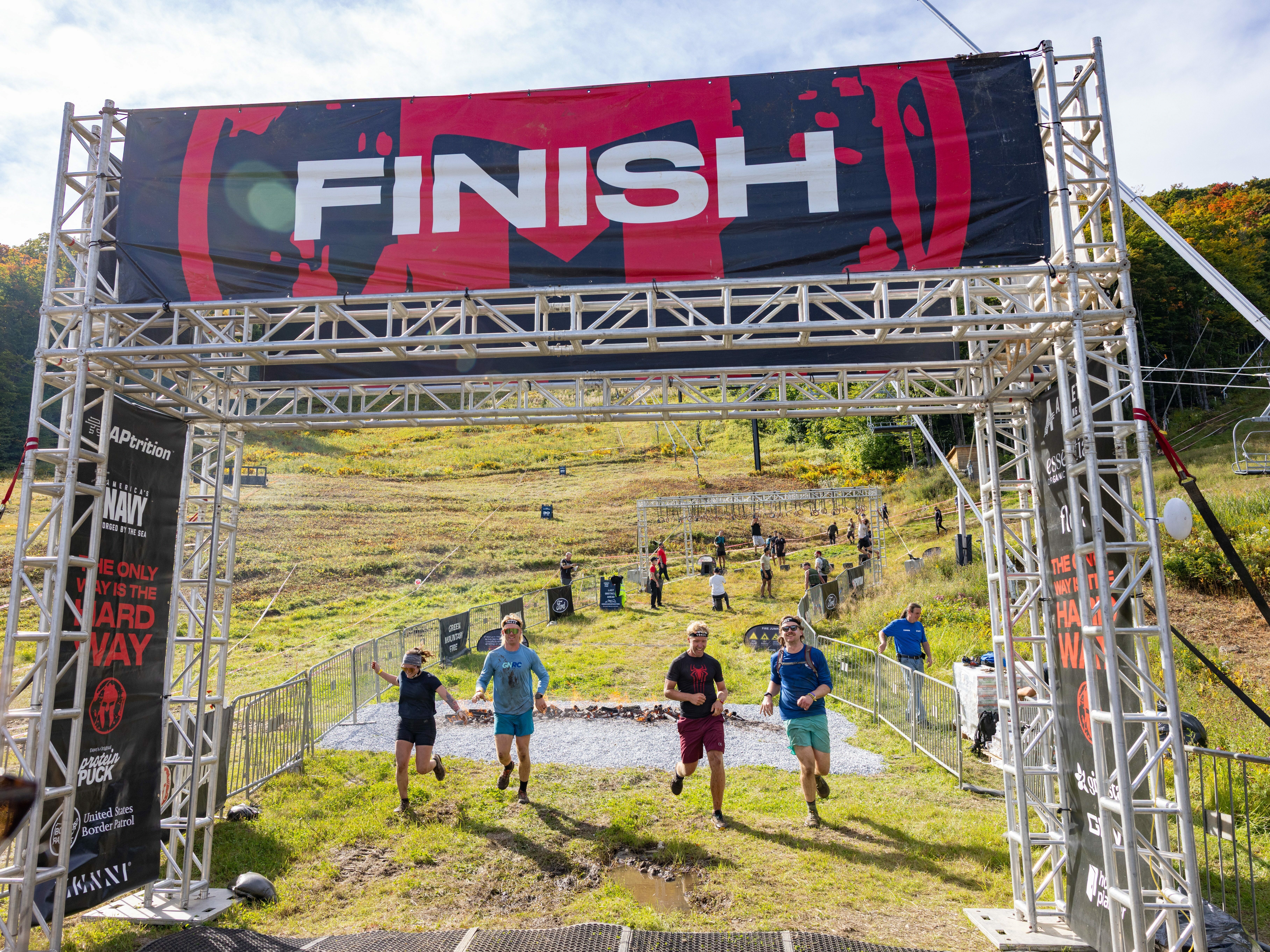 Runners crossing a finish line at an outdoor event on a sunny day.