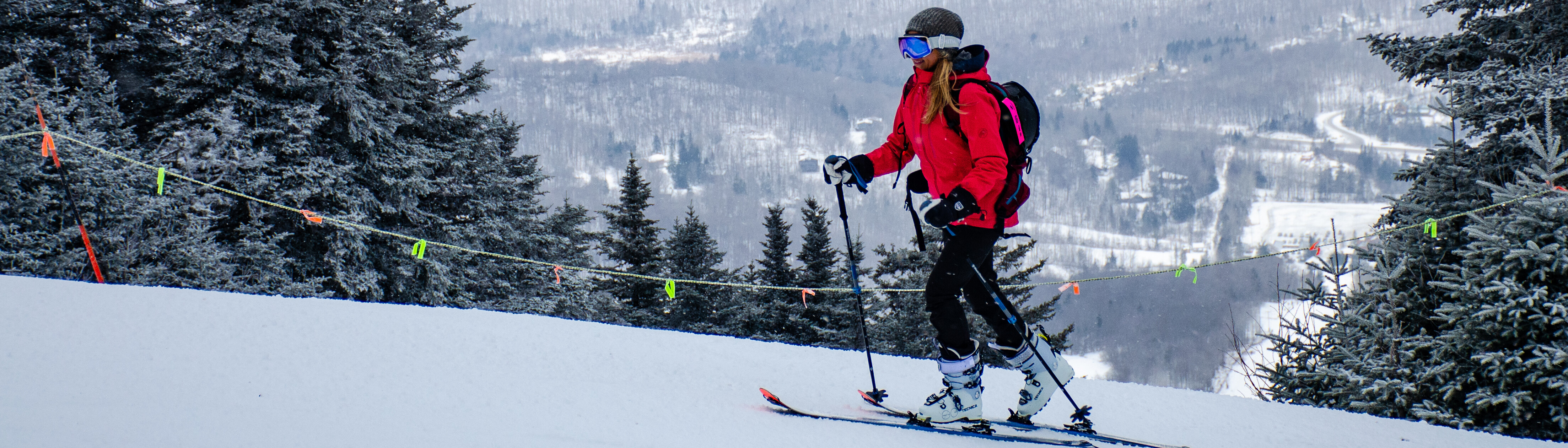 A skier dressed in bright red descends a snowy slope surrounded by trees.