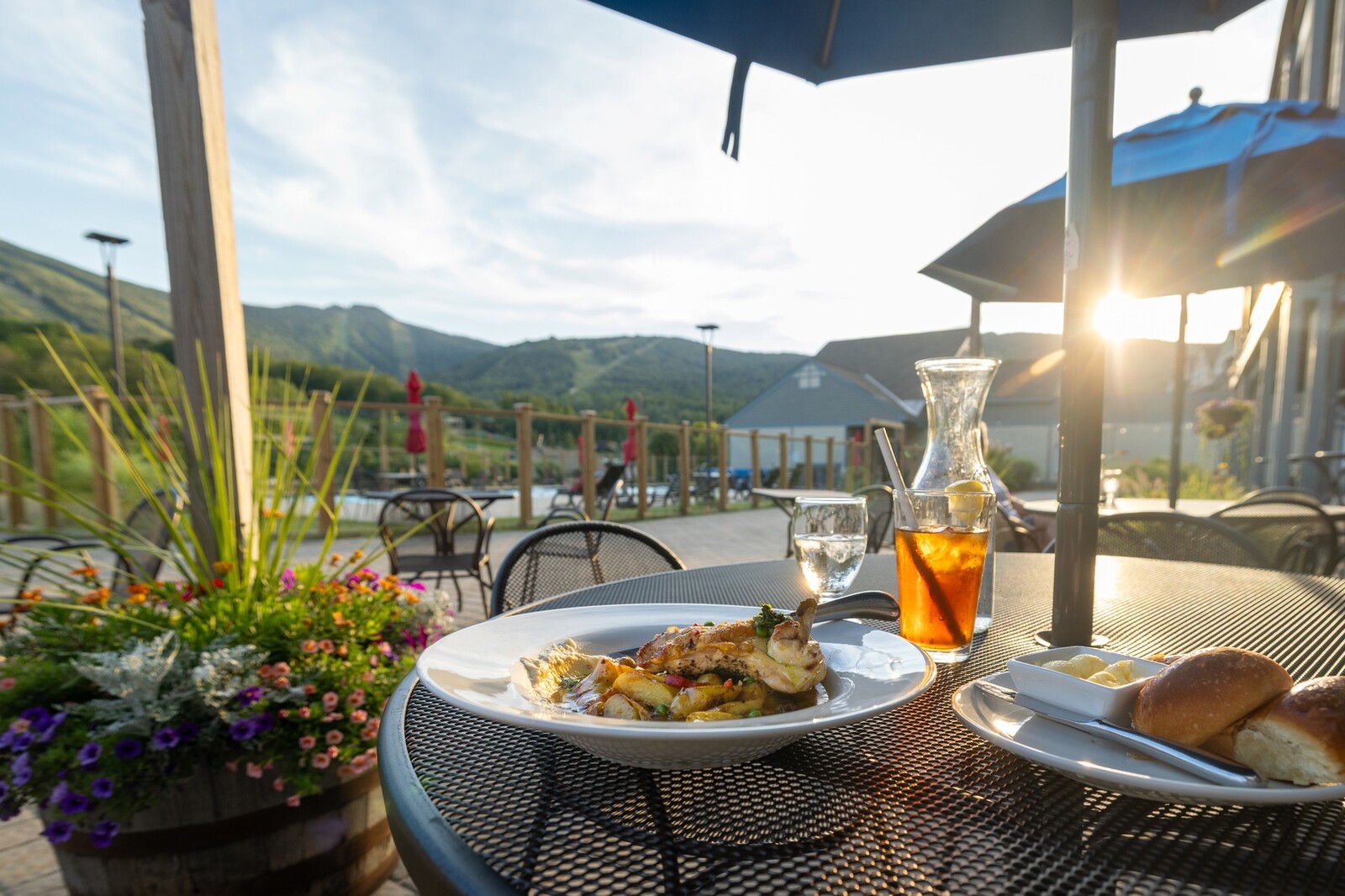 A table set outside with a plate of food, drinks, and scenic mountains in the background.