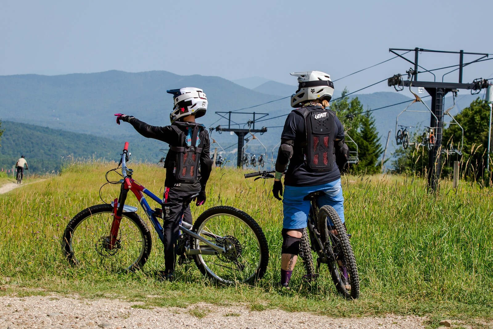 Two mountain bikers discussing a trail while overlooking a scenic landscape and ski lift.