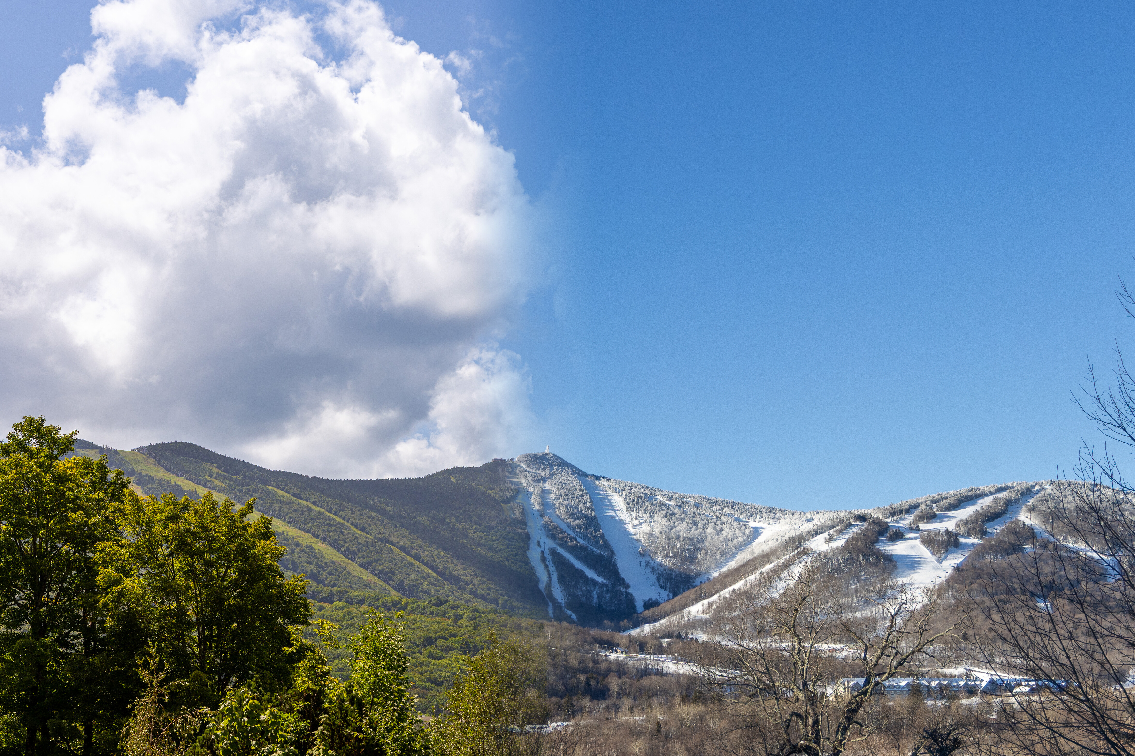 Split image of a mountain in summer (left) and winter (right) under contrasting skies.