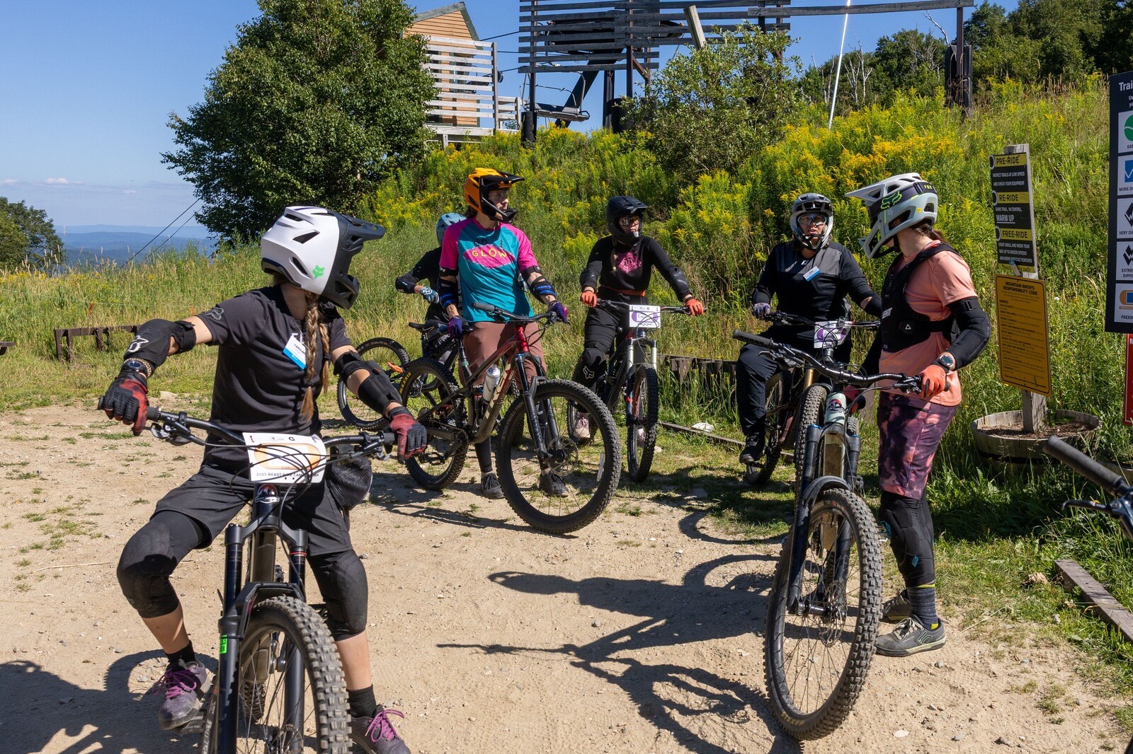 A group of five mountain bikers gathers on a trail, discussing their ride.