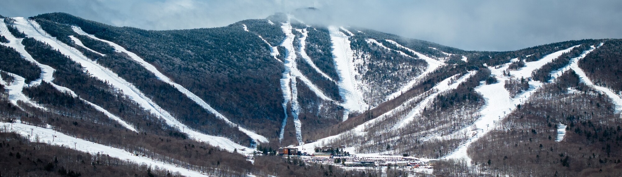 Ski slopes and a lodge nestled among snow-covered mountains under a cloudy sky.