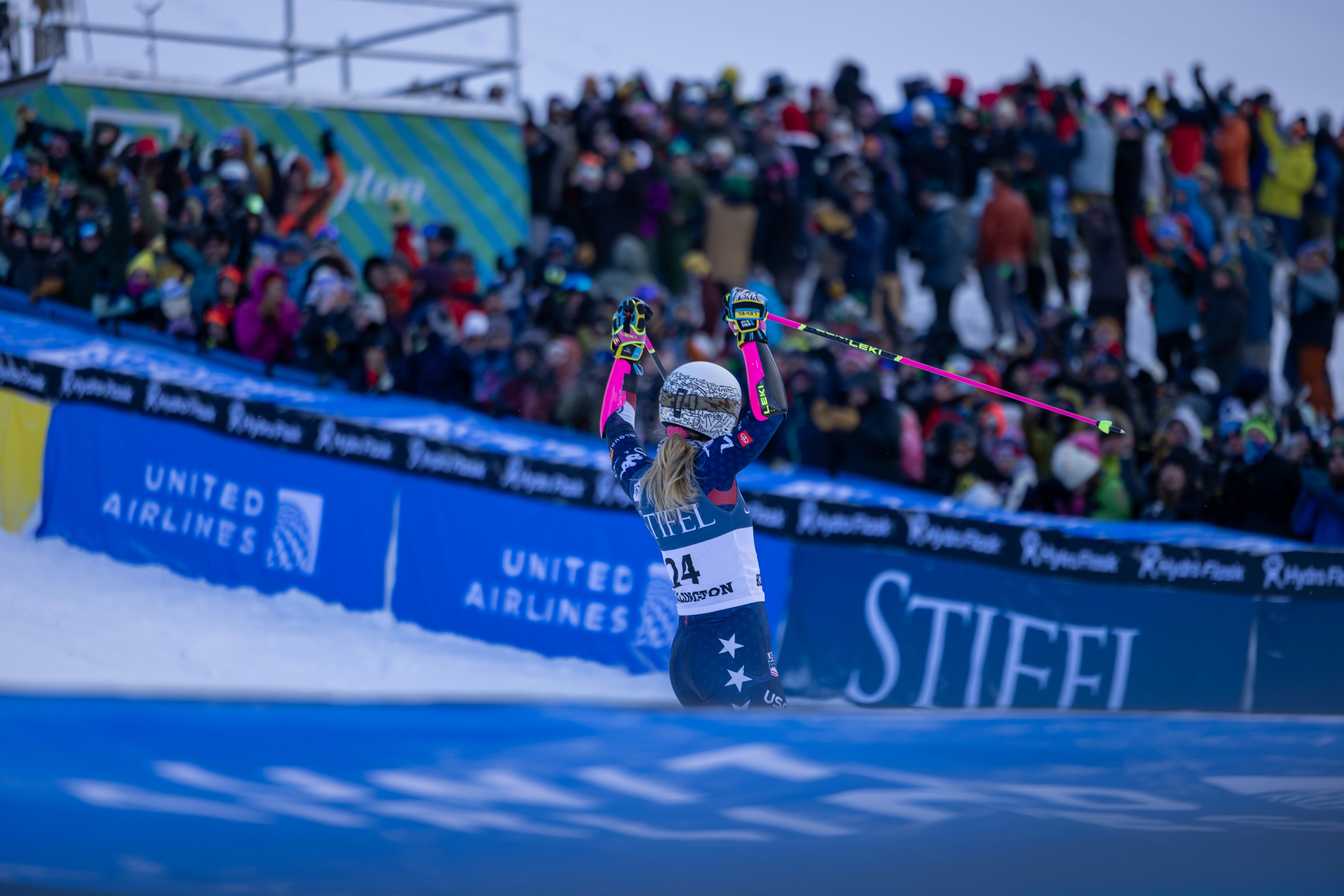 A skier celebrates with raised arms in front of a cheering crowd at a snowy event.