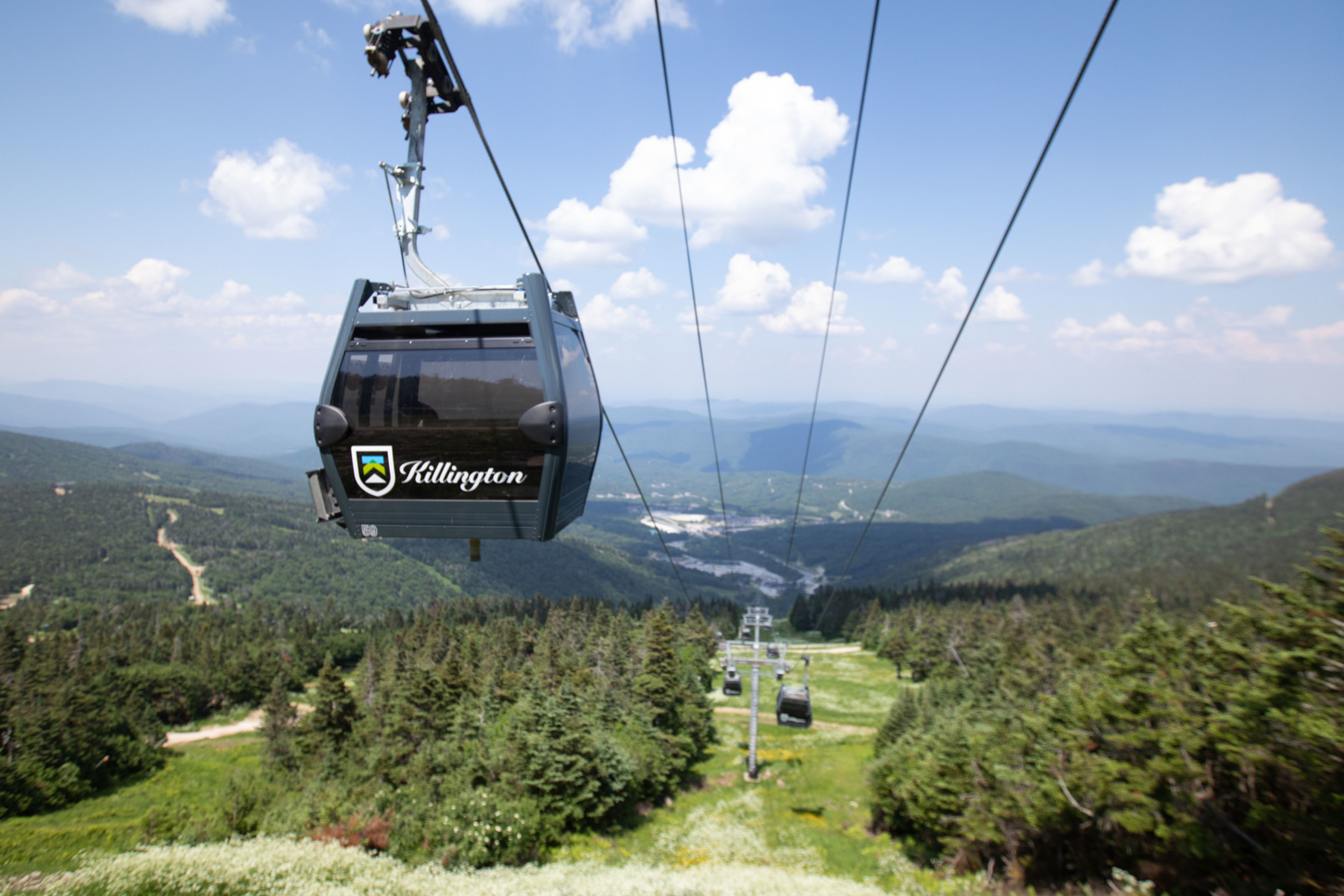A gondola ascends a mountain with scenic views of trees and valleys below.