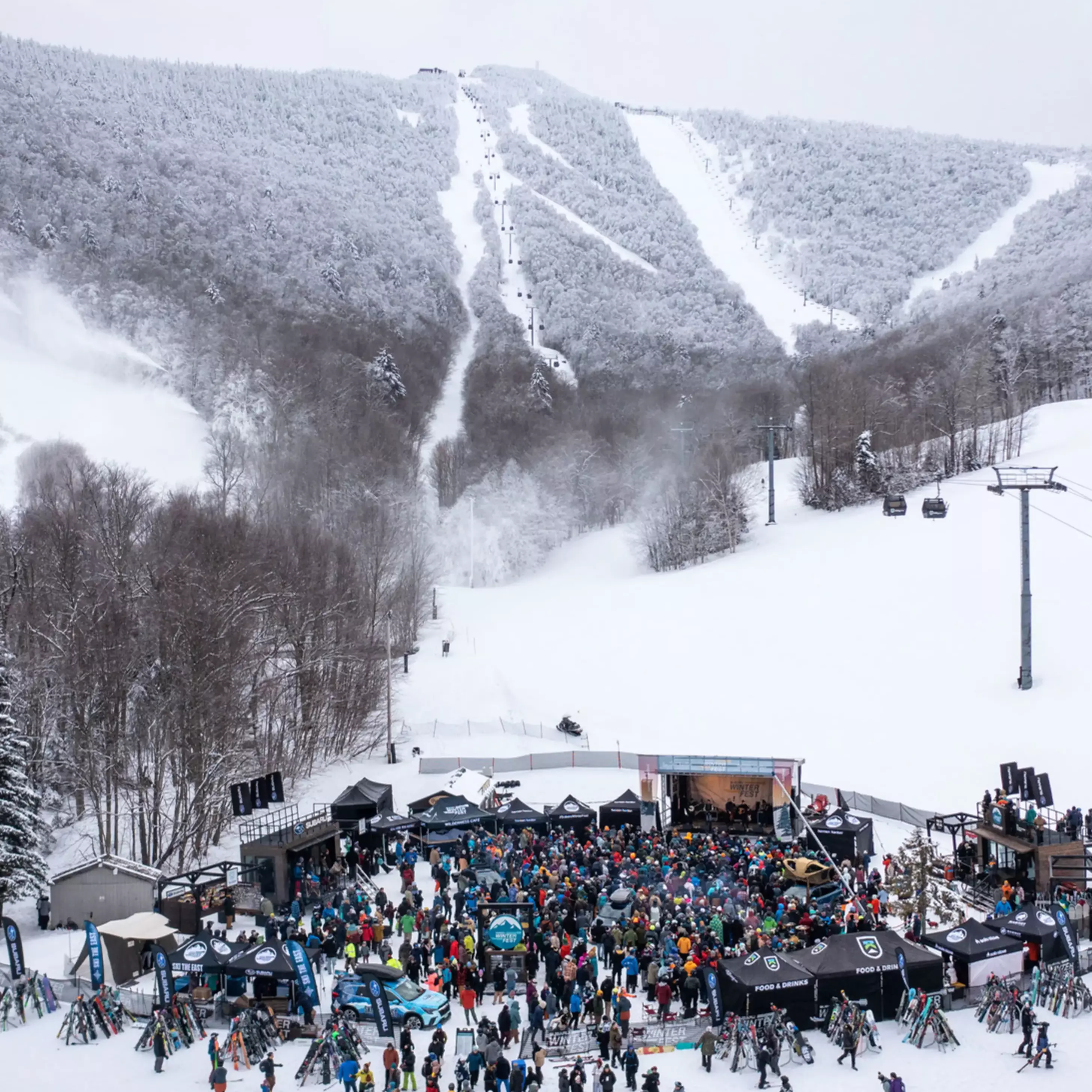 Crowd gathered at a ski resort with snow-covered mountains in the background.