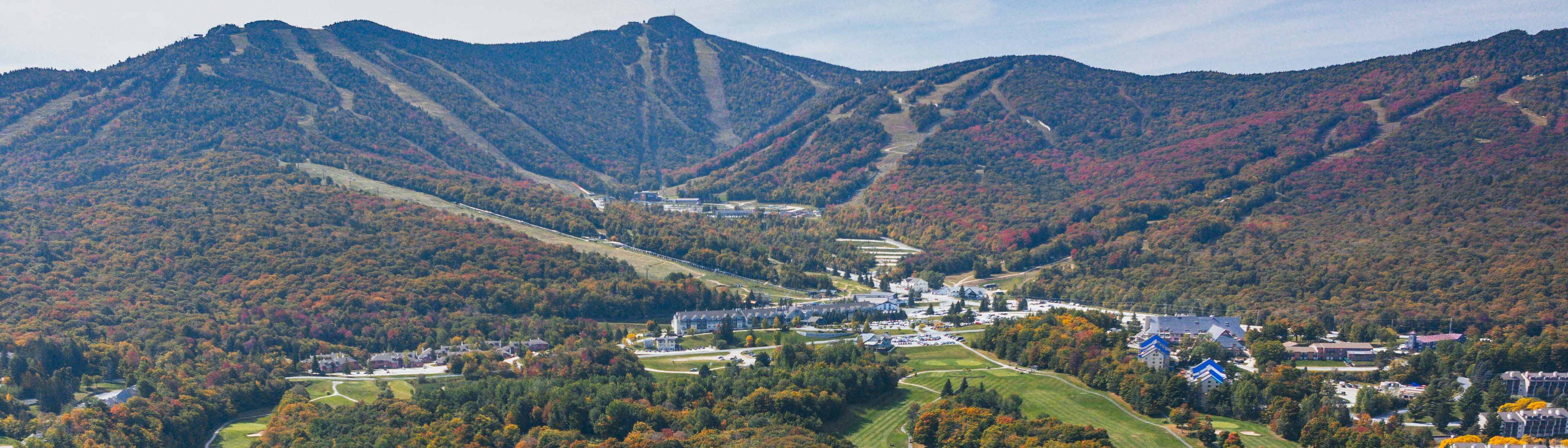 Aerial view of mountains with colorful autumn foliage and a resort area below.