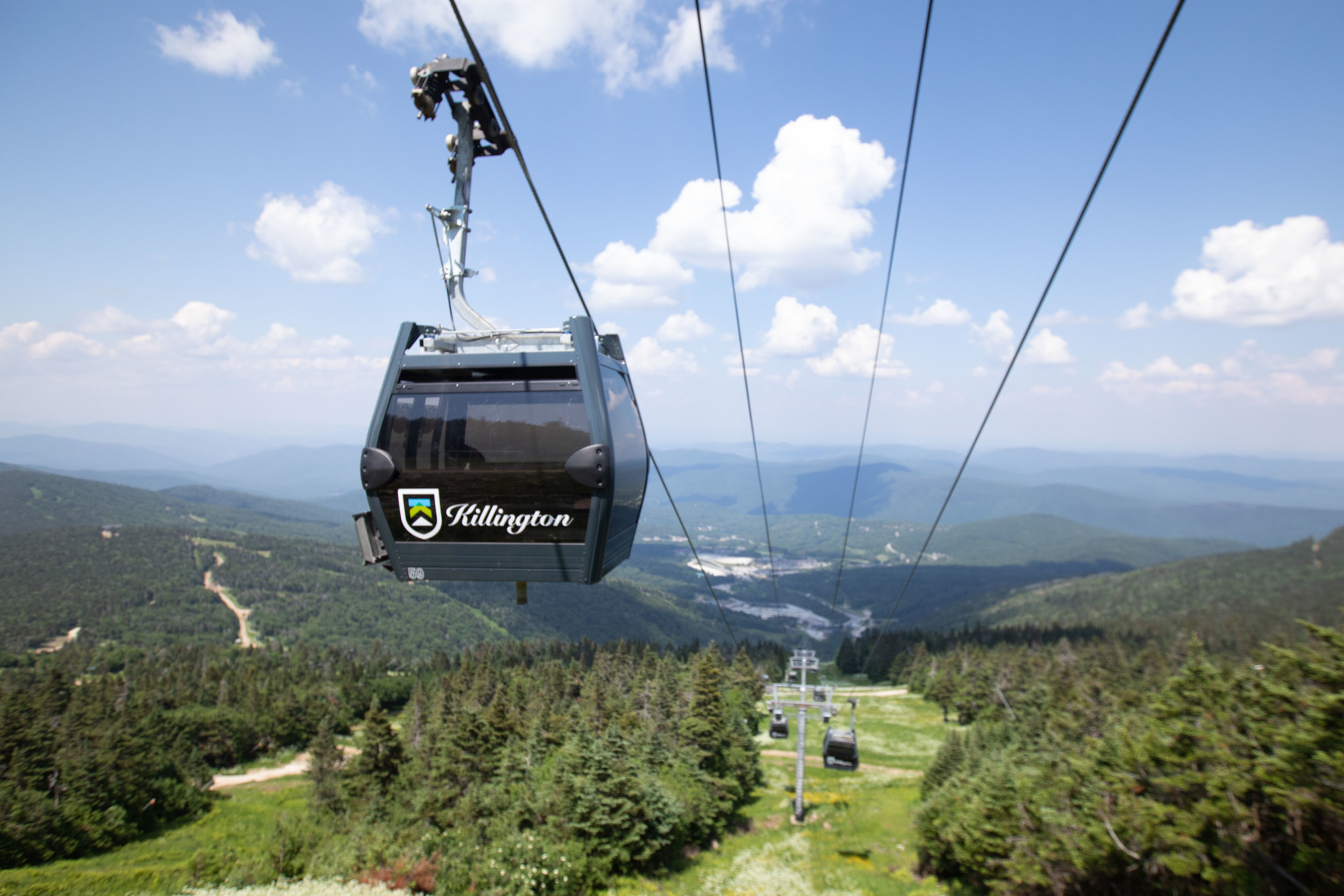 A Killington gondola travels above lush mountains under a blue sky.