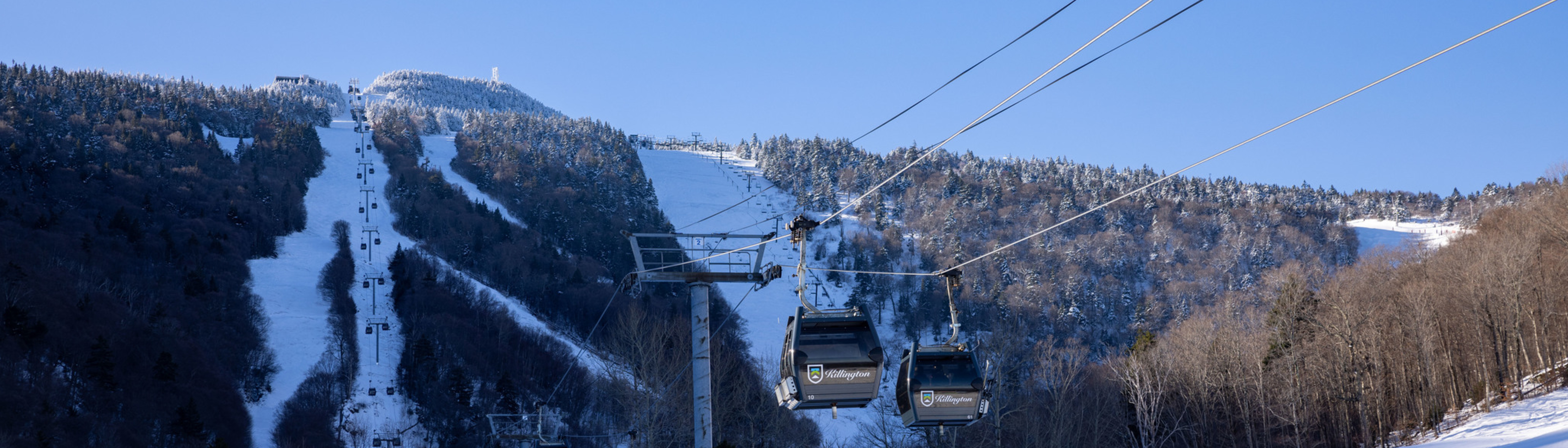 A snowy mountain landscape with ski gondolas ascending a slope under a clear blue sky.
