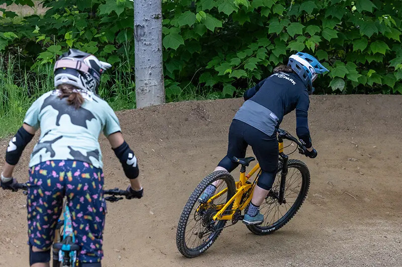 Two cyclists riding on a dirt track in a green forested area.