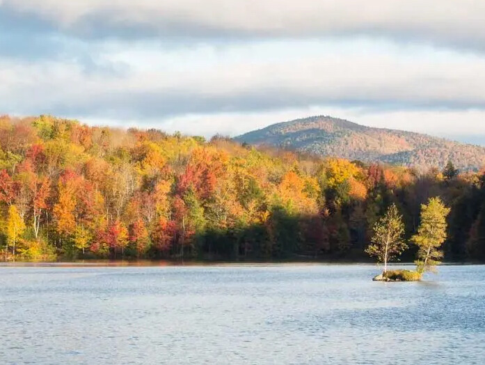 Vibrant autumn trees surround a serene lake with a small island in the foreground.