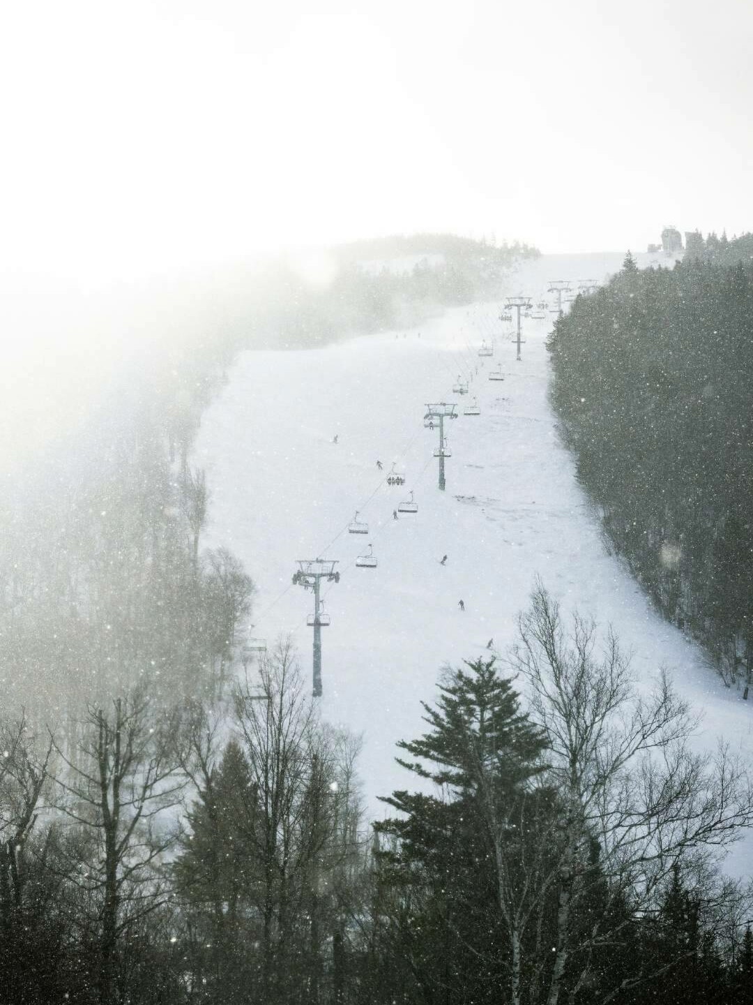 Skiers on a snowy slope with ski lifts against a foggy backdrop.