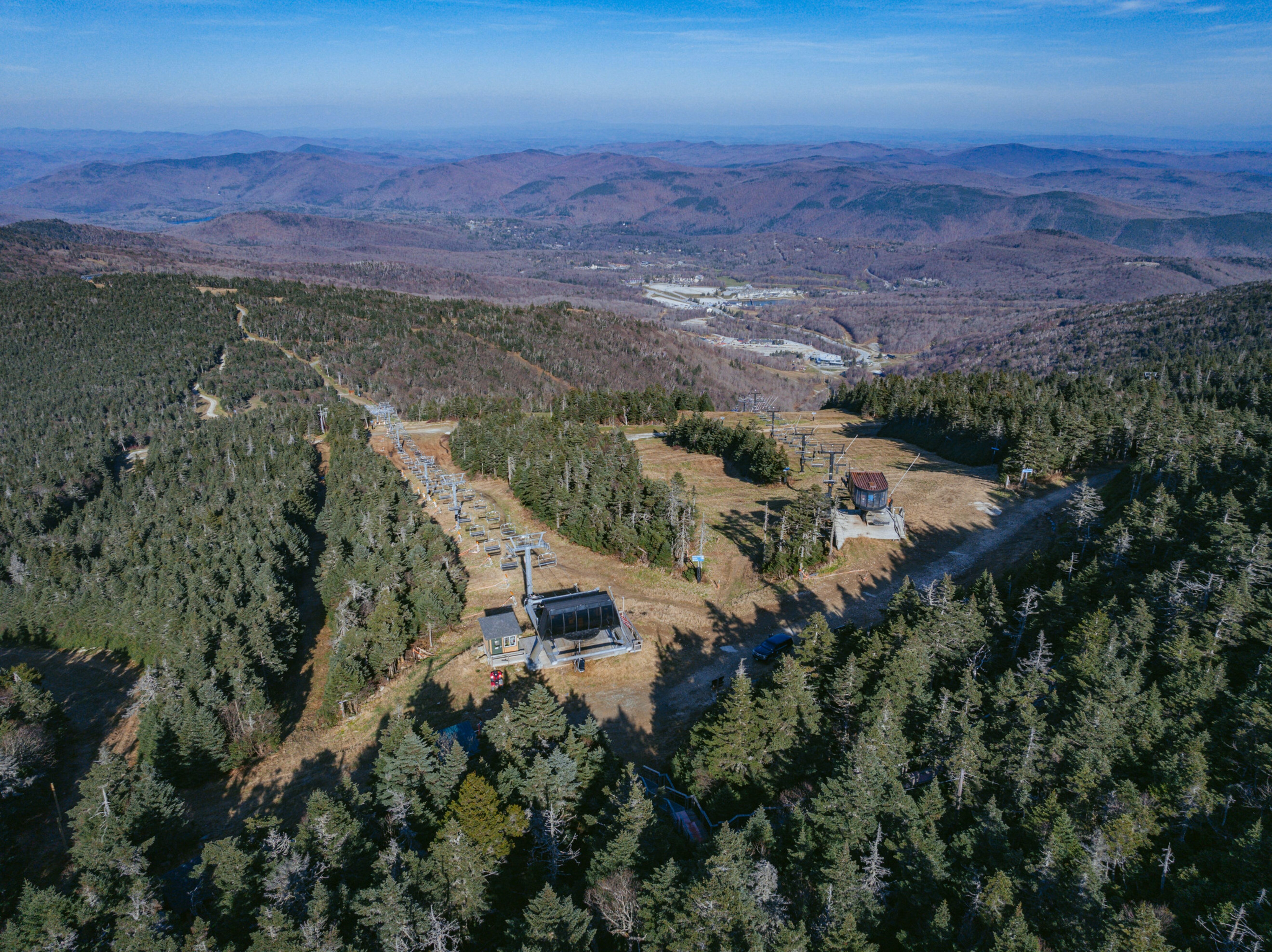 Aerial view of a ski resort with chairlifts, forests, and rolling hills in the background.