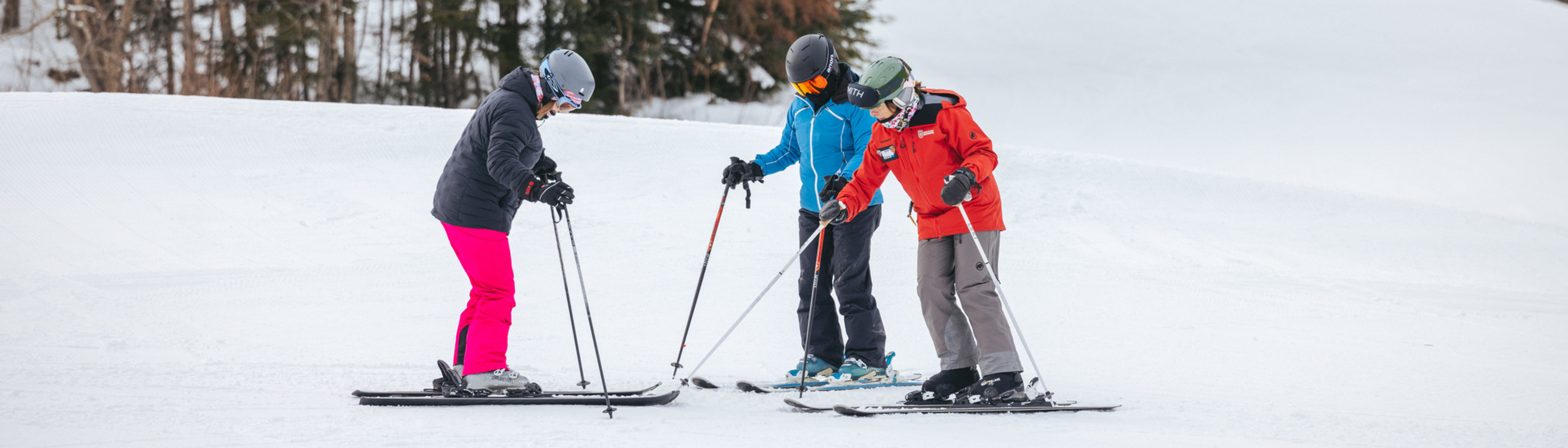 Three skiers practice on the slopes, wearing colorful winter gear in a snowy landscape.