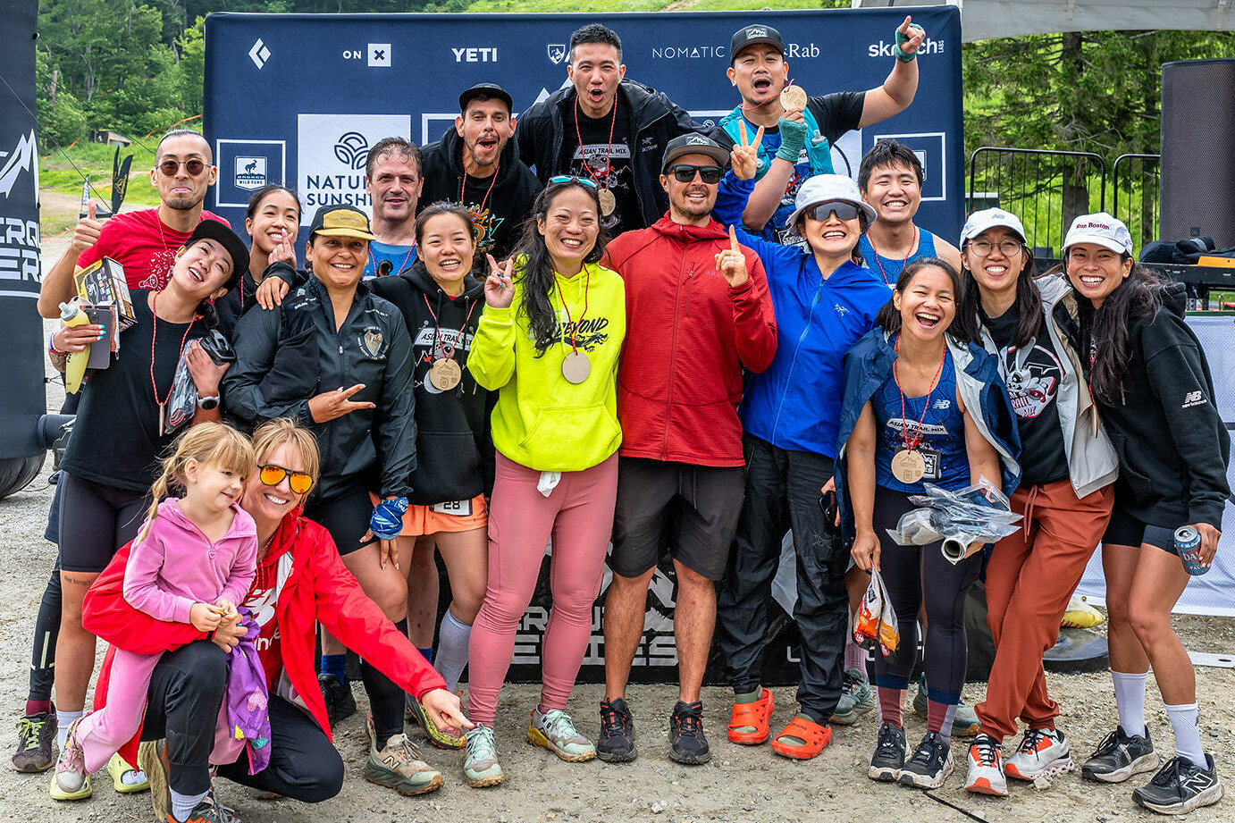 Group photo of diverse participants celebrating with medals at an outdoor event.