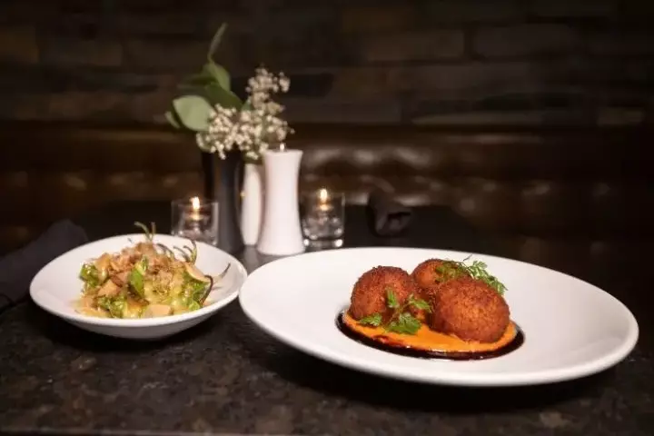 Plated dishes featuring croquettes, sauce, and a side salad on a dark table.