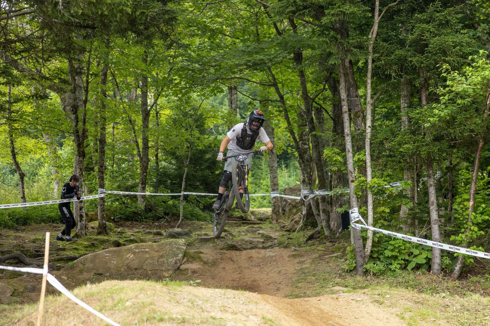 Mountain biker jumps over a path with trees in the background during a race.