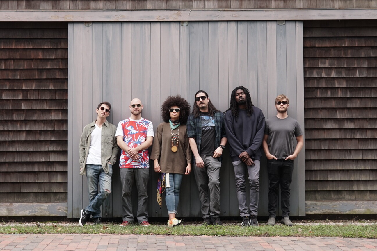 A group of six people poses in front of a wooden wall, showcasing diverse styles.