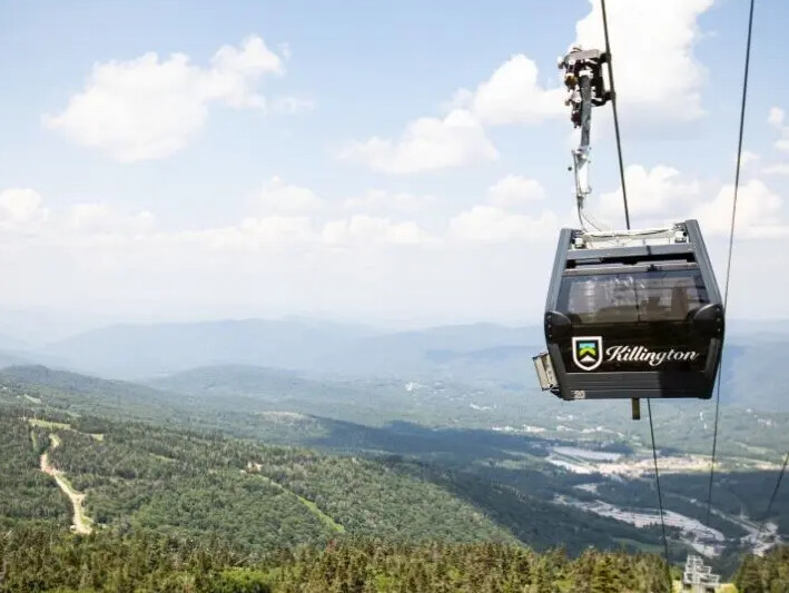 A gondola with a "Killington" logo travels over a mountainous landscape.