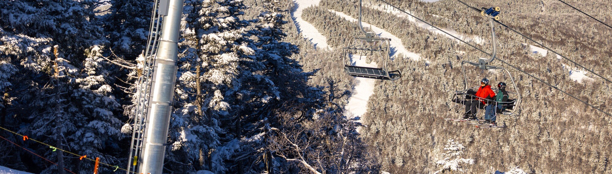 Skiers on a lift overlooking snow-covered trees and slopes.