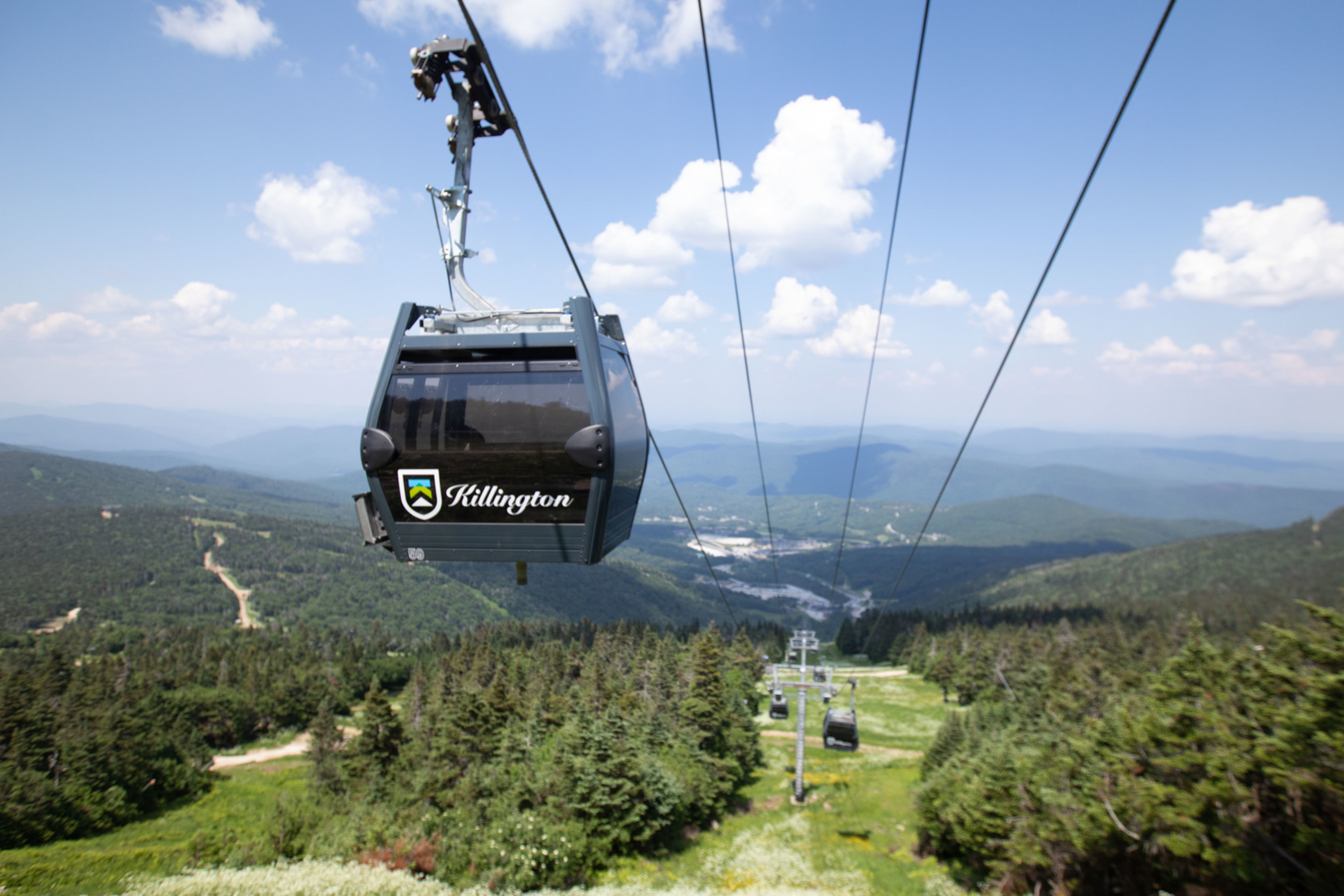 A gondola cable car from Killington, overlooking green mountains and a blue sky.