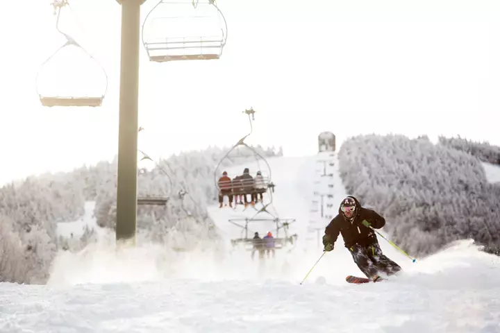 Skier racing down a slope with a ski lift and snowy landscape in the background.