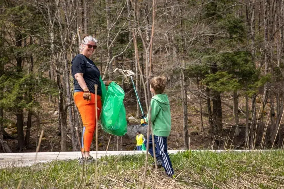 Woman and child pick up litter together in a forested area.